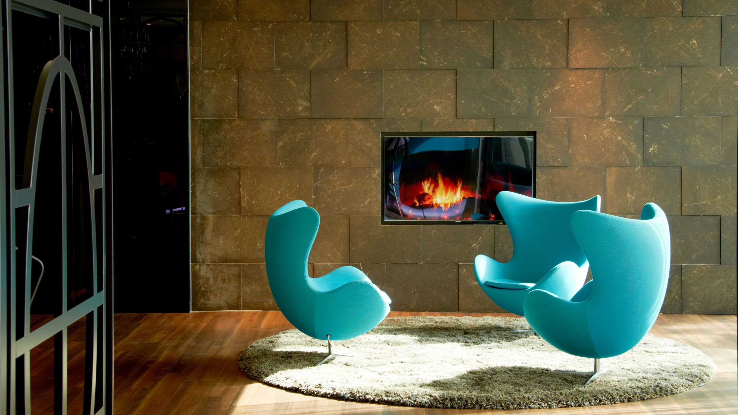 Hotel Amsterdam Motel One drei Egg Chairs vor einem TV mit Kaminbild