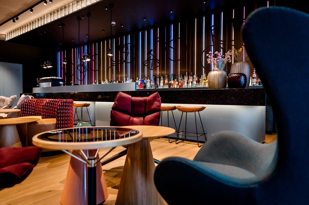 Moderne Bar mit stilvoller Beleuchtung, gemütlichen Sesseln und Hockern, warmem Holzboden und dekorativen Vasen schafft ein einladendes Ambiente zum Entspannen und Genießen von Getränken.