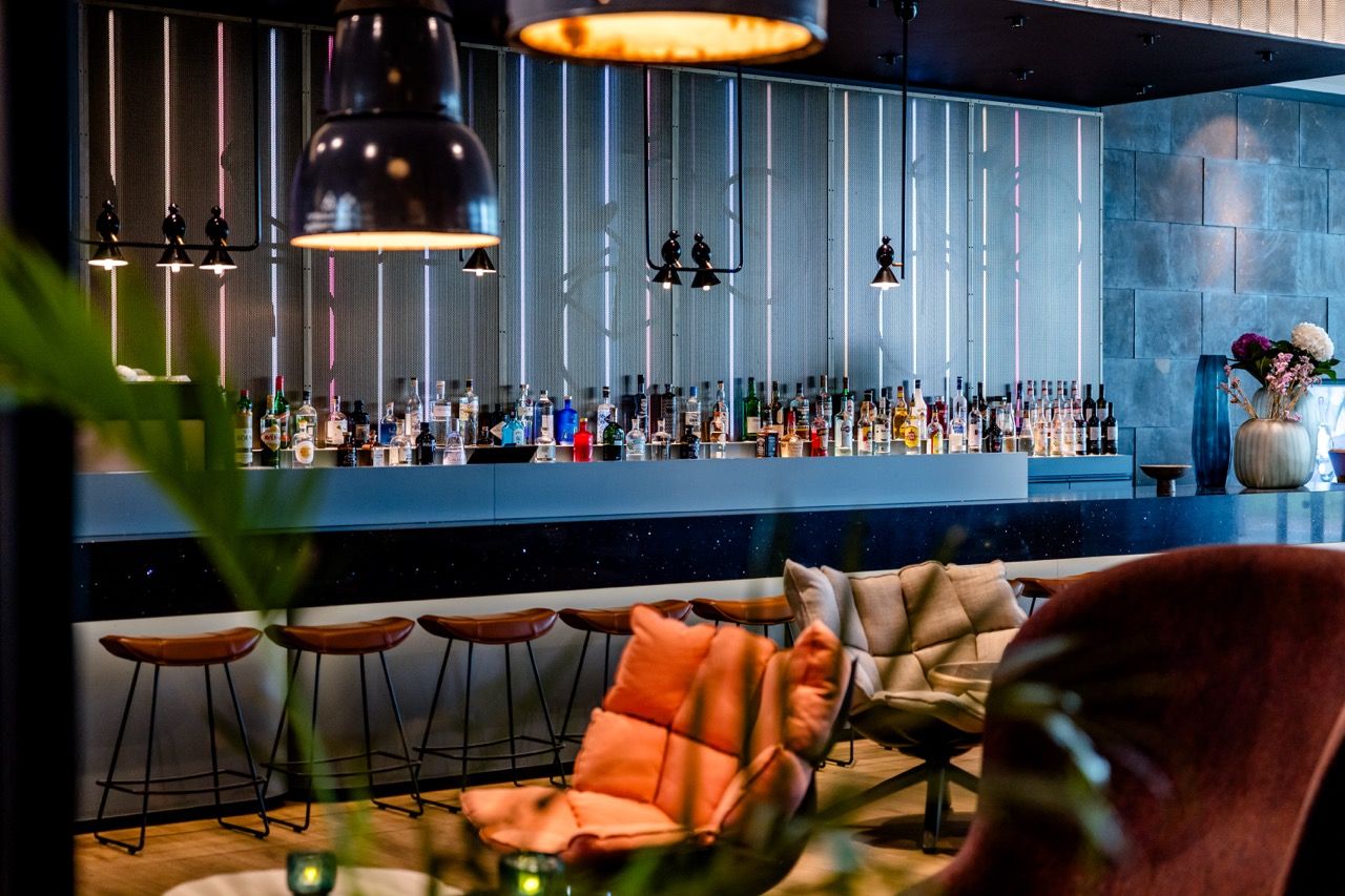 Moderne Hotelbar mit stilvoller Beleuchtung, bequemen Sesseln in warmen Farben und einer großen Auswahl an Getränken hinter dem Tresen, ideal für entspannte Abende.