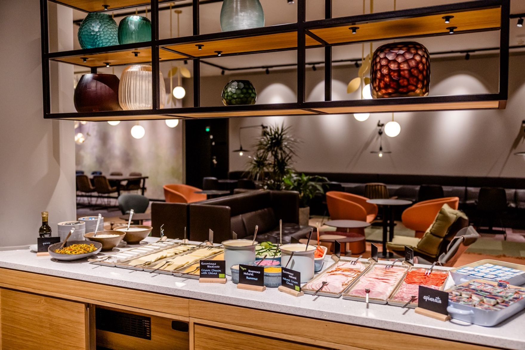 Buffet mit vielfältigen Aufschnitt-, Käse- und Fischplatten in stilvollem Lounge-Bereich, gemütliche Sitzgelegenheiten im Hintergrund, warme Beleuchtung schafft ein einladendes Ambiente.