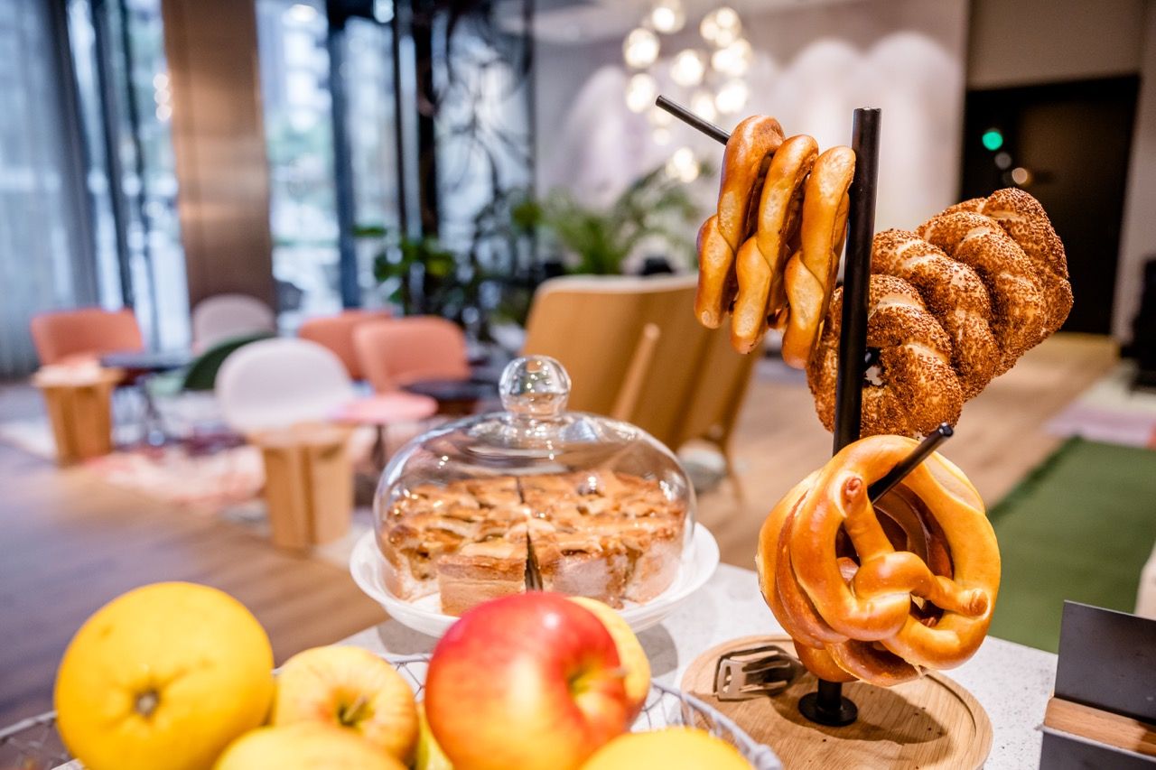 Frisch gebackene Laugenbrezeln und ein gedeckter Apfelkuchen stehen im Frühstücksbereich bereit, um Gäste mit hausgemachten Snacks willkommen zu heißen.