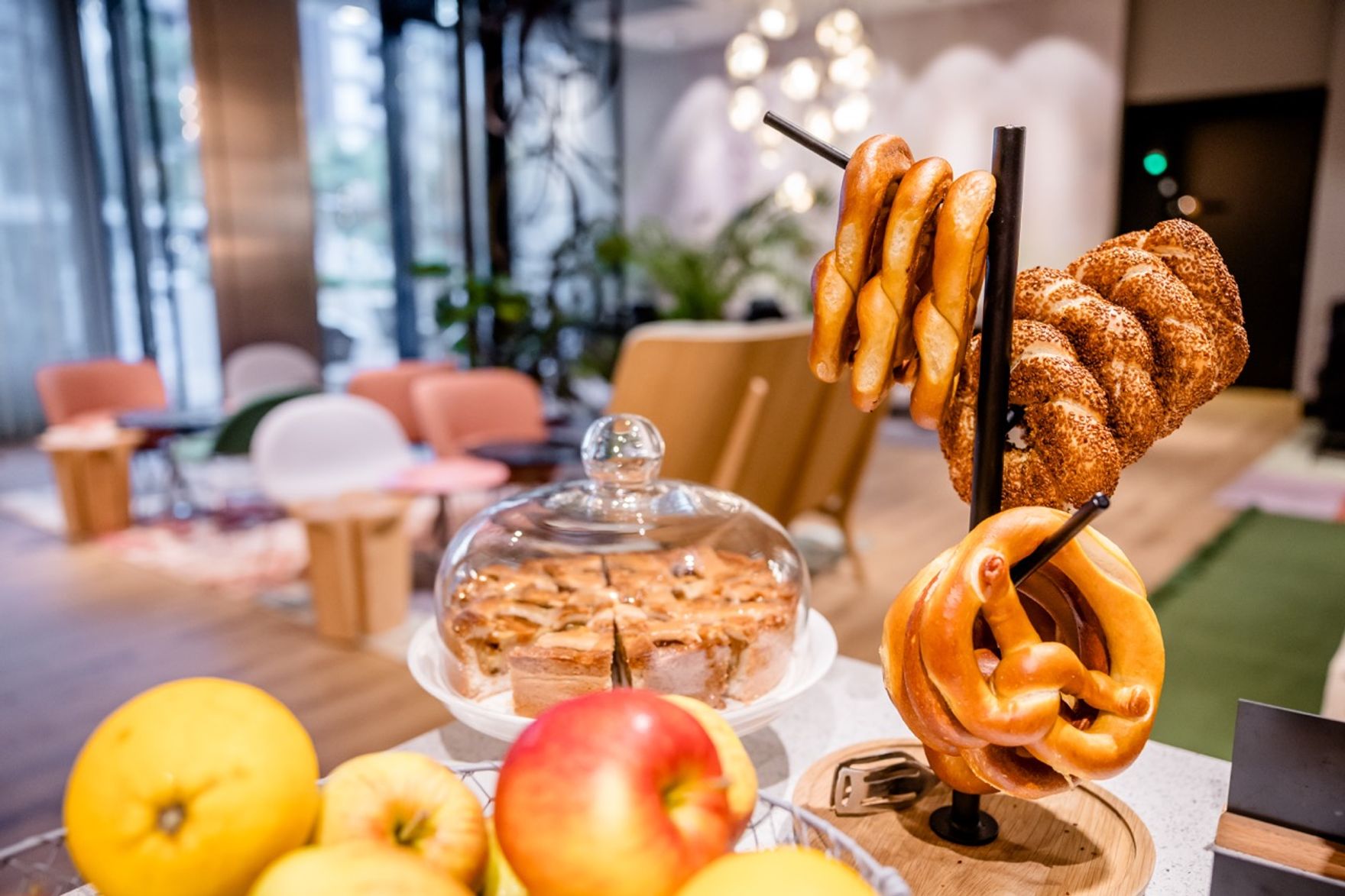 Frisch gebackene Laugenbrezeln und ein gedeckter Apfelkuchen stehen im Frühstücksbereich bereit, um Gäste mit hausgemachten Snacks willkommen zu heißen.