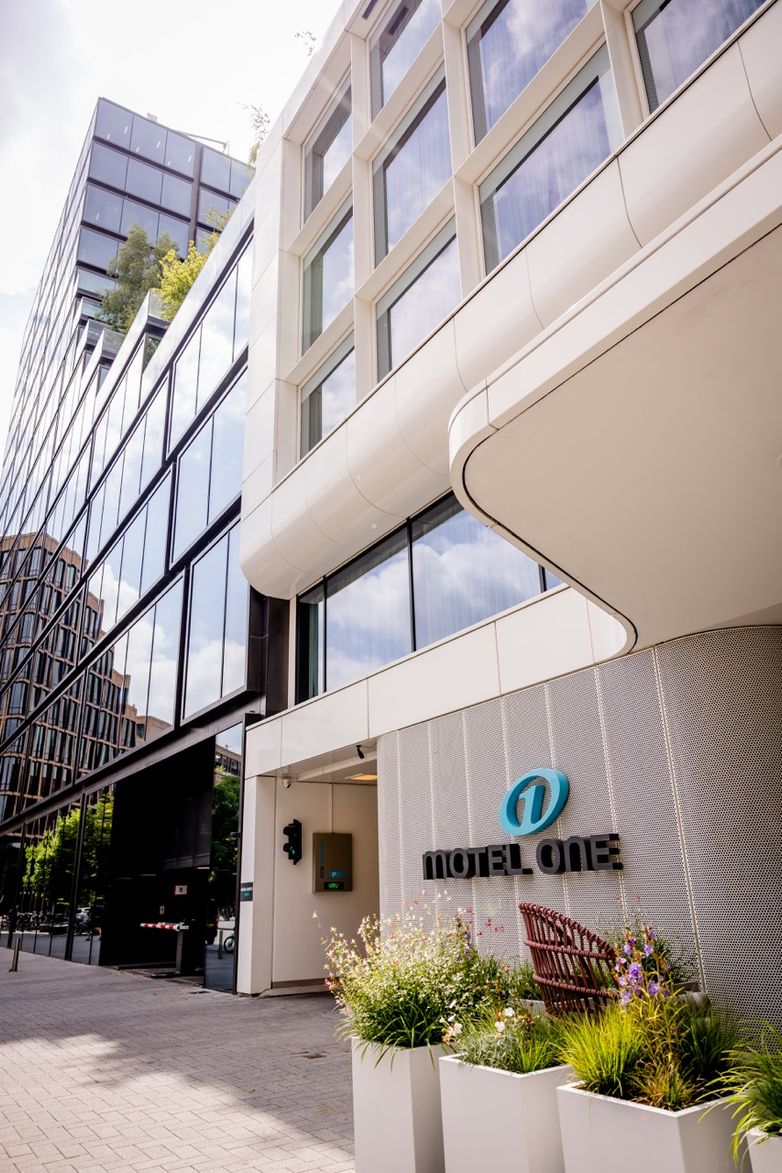 Außenansicht eines modernen Hotels mit großen Glasfenstern, klaren Linien und einem Eingangsbereich mit grünen Pflanzen, der ein einladendes Ambiente für Geschäfts- und Freizeitreisende schafft.