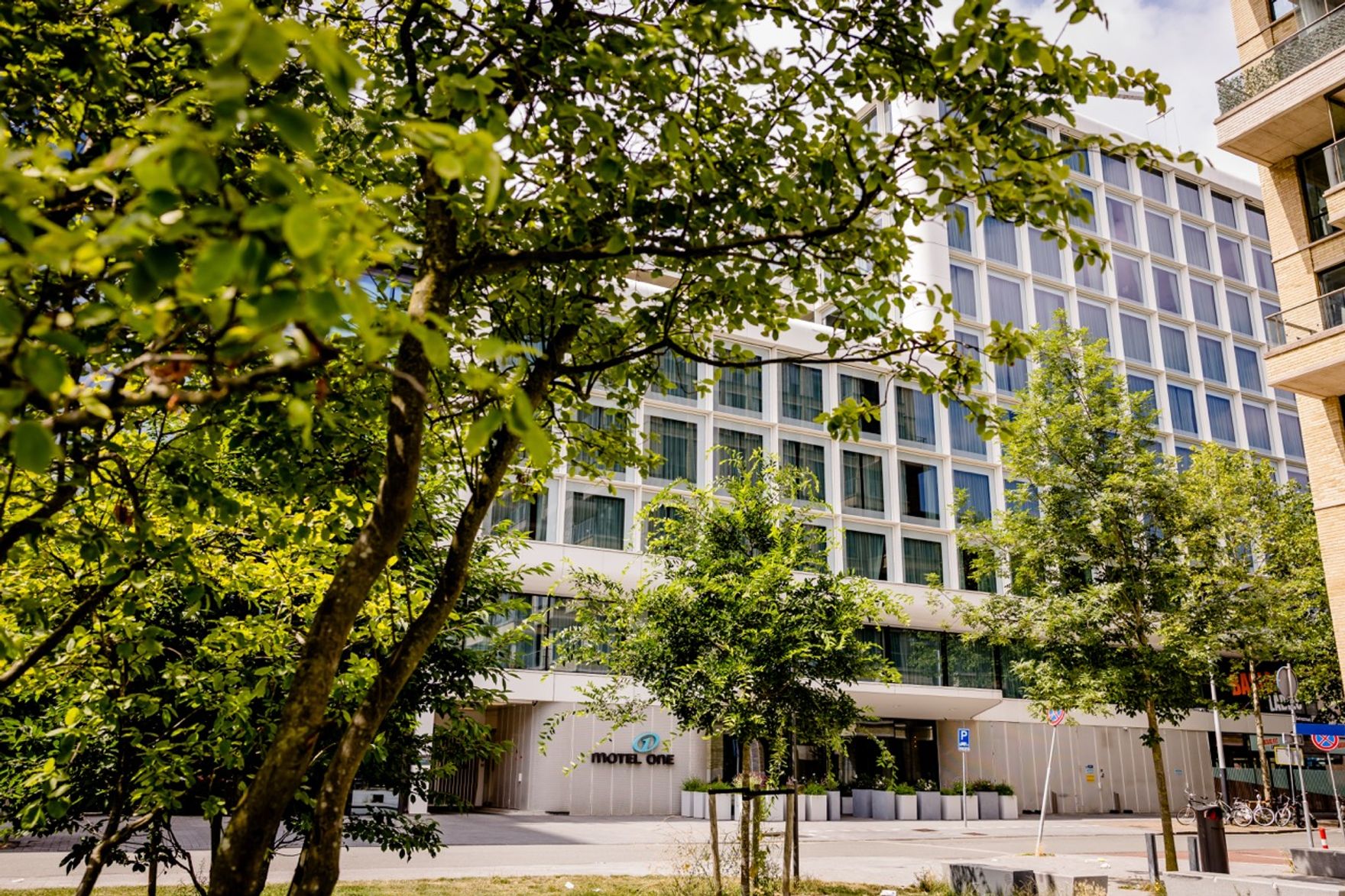 Blick auf die moderne Fassade des Hotels mit großen Fenstern, umgeben von grünen Bäumen und einem gepflegten Außenbereich, der eine ruhige und einladende Atmosphäre schafft.
