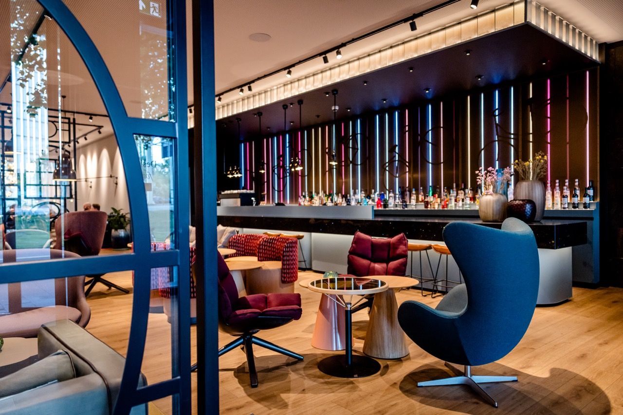 Moderne Hotelbar mit stilvollen Sesseln und Sofas, eleganter Beleuchtung und einer langen Bar mit vielfältiger Getränkeauswahl, die zum Entspannen und geselligen Beisammensein einlädt.