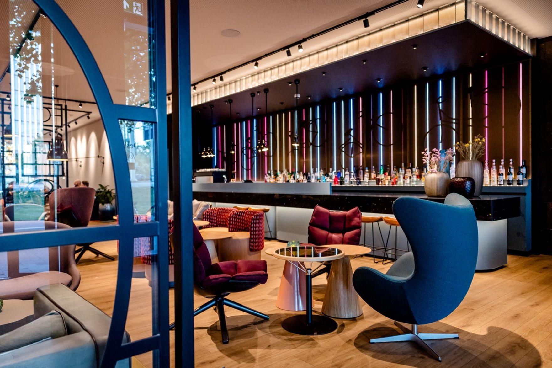 Moderne Hotelbar mit stilvollen Sesseln und Sofas, eleganter Beleuchtung und einer langen Bar mit vielfältiger Getränkeauswahl, die zum Entspannen und geselligen Beisammensein einlädt.