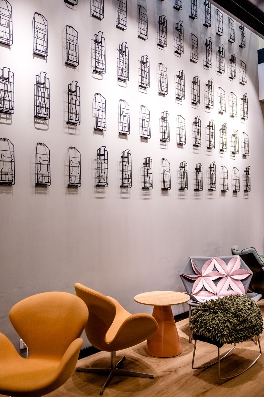 Moderne, gemütliche Sitzecke mit orangen Sesseln, kleinem Holztisch und kreativem Pflanzenhocker vor heller Wand mit dekorativen, schwarzen Drahtregalen in gleichmäßigem Muster.