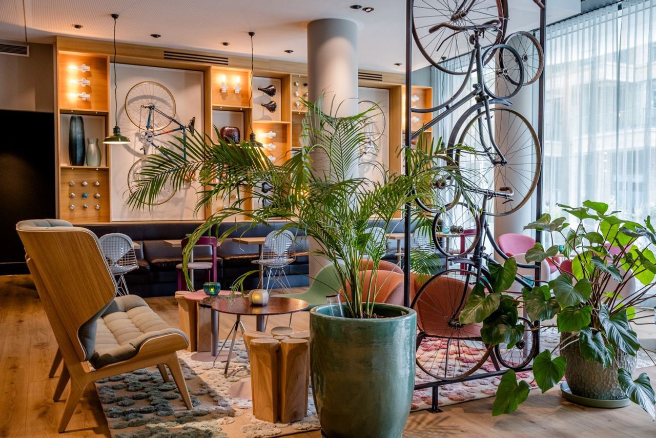 Helle Lounge mit modernen Sitzmöbeln, großen Pflanzen und dekorativ an der Wand und von der Decke hängenden Fahrrädern, die eine entspannte und stilvolle Atmosphäre schaffen.