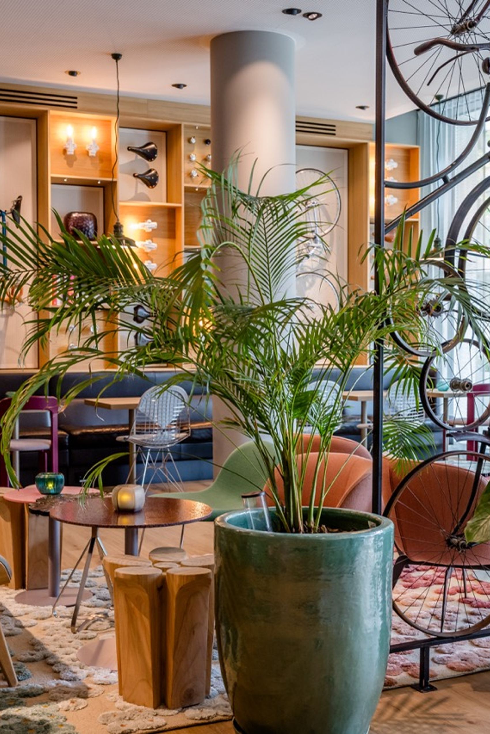 Helle Lounge mit modernen Sitzmöbeln, großen Pflanzen und dekorativ an der Wand und von der Decke hängenden Fahrrädern, die eine entspannte und stilvolle Atmosphäre schaffen.
