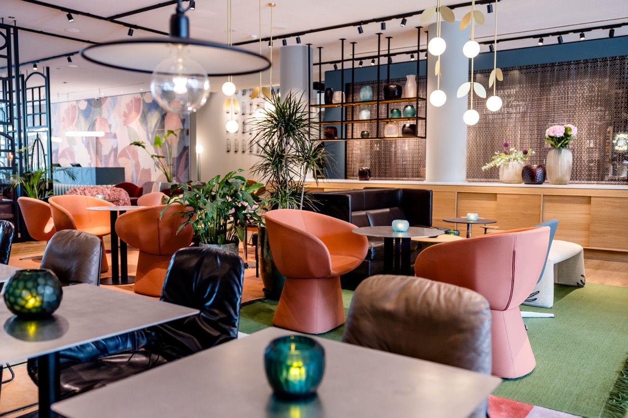 Moderner Hotel-Lounge-Bereich mit stilvollen Sesseln, Tischen, stimmungsvoller Beleuchtung und grünen Pflanzen, der eine entspannte Atmosphäre zum Verweilen und Gespräche bietet.