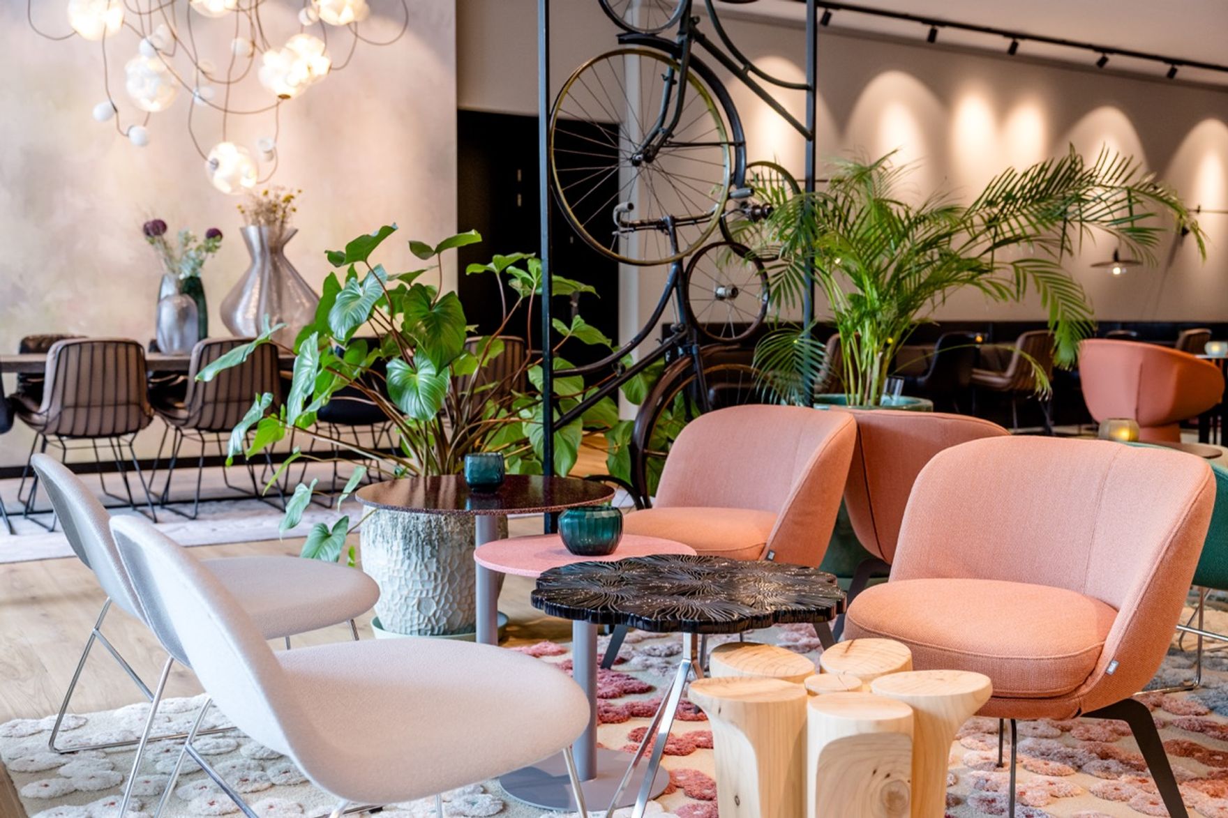 Gemütlicher Lounge-Bereich mit bequemen Sesseln, modernen Holztischen, grünen Pflanzen und stilvoller Beleuchtung, ideal zum Entspannen und Verweilen in einem eleganten, einladenden Ambiente.