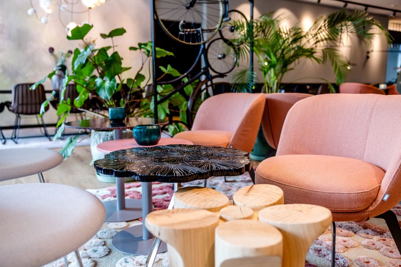 Gemütliche Lounge-Ecke mit pastellfarbenen Sesseln, künstlerischem Holztisch und viel Grün, ideal für entspannte Gespräche und kleine Auszeiten im stilvollen Ambiente.