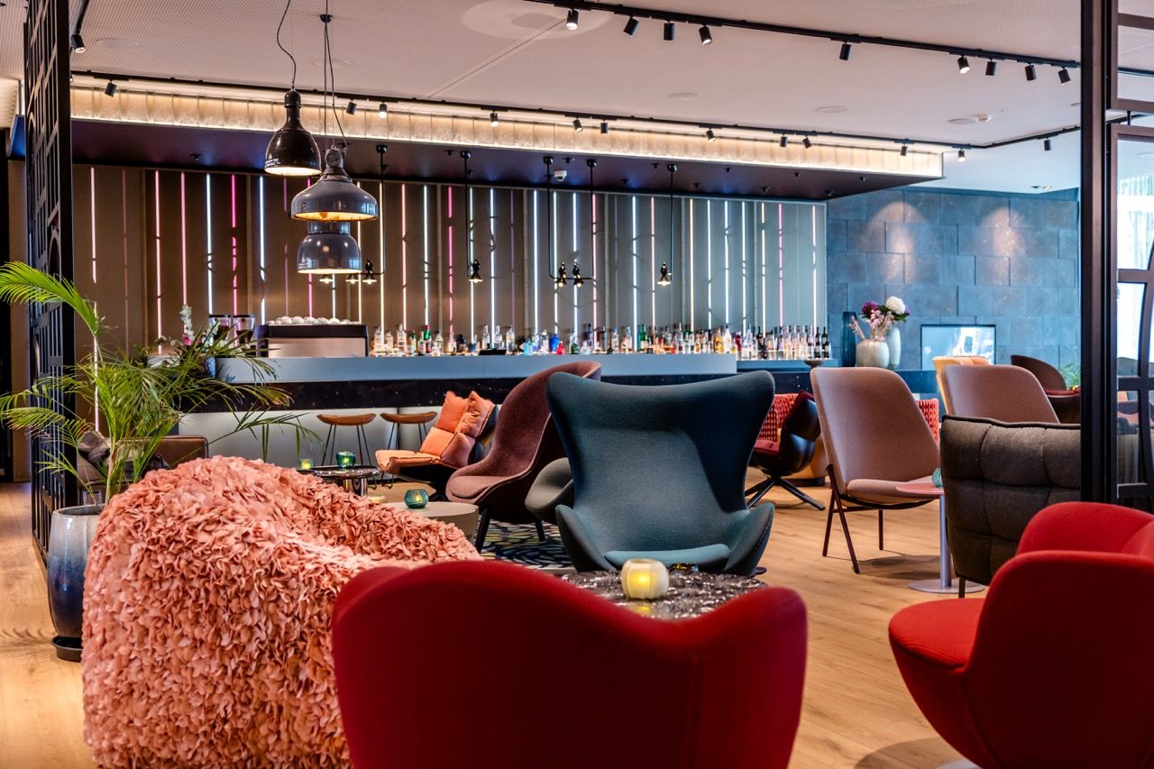 Moderne Hotelbar mit stilvoller Atmosphäre, bequemen Sesseln in verschiedenen Farben und gemütlicher Beleuchtung, ideal zum Entspannen und geselligen Beisammensein.