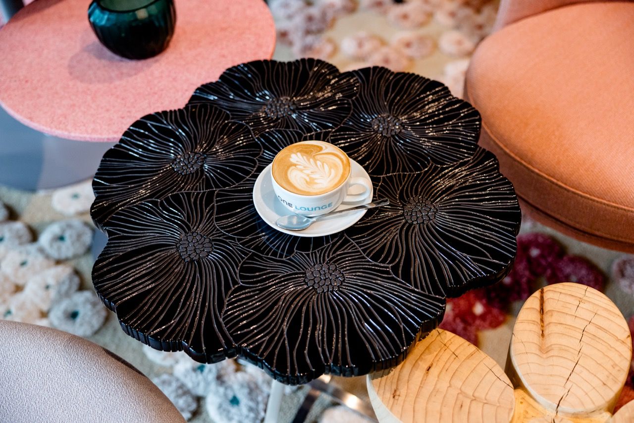 Schwarzer, kunstvoll gestalteter Couchtisch mit Kaffeetasse und Latte Art. Angenehme, moderne Atmosphäre mit gemütlichen Sitzgelegenheiten im Hintergrund. Ideal für entspannte Momente oder geselliges Beisammensein.