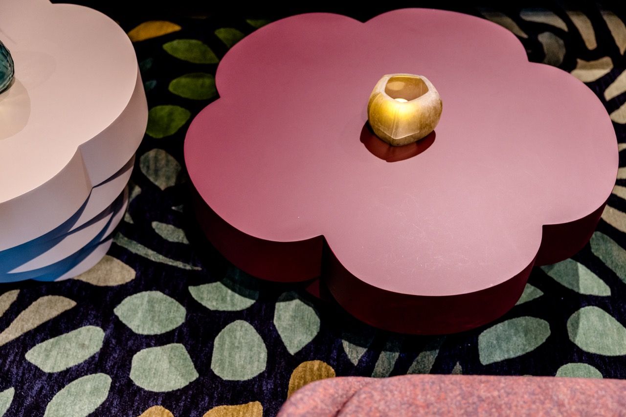 Zwei stilvolle Blumentischchen in Weiß und Rosa stehen auf einem modernen, gemusterten Teppich. Auf dem rosa Tisch liegt ein kleines, rundes Dekoelement, das eine warme und gemütliche Atmosphäre schafft.