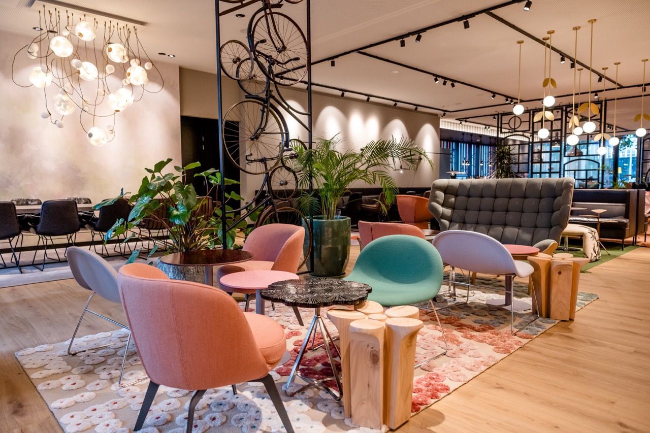 Moderne Lounge mit farbenfrohen, bequemen Sesseln, stilvollen Tischen und grünen Pflanzen, offen und einladend gestaltet, ideal zum Entspannen und geselligen Beisammensein in stilvollem Ambiente.
