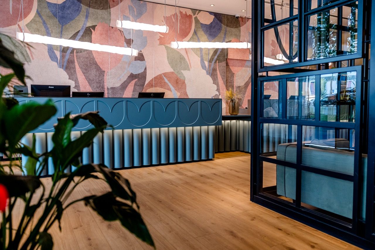 Moderner Hotel-Empfang mit stilvollem blauen Empfangstresen, warmem Holzboden und dekorativer Wandgestaltung in sanften Farben für ein einladendes Ambiente.