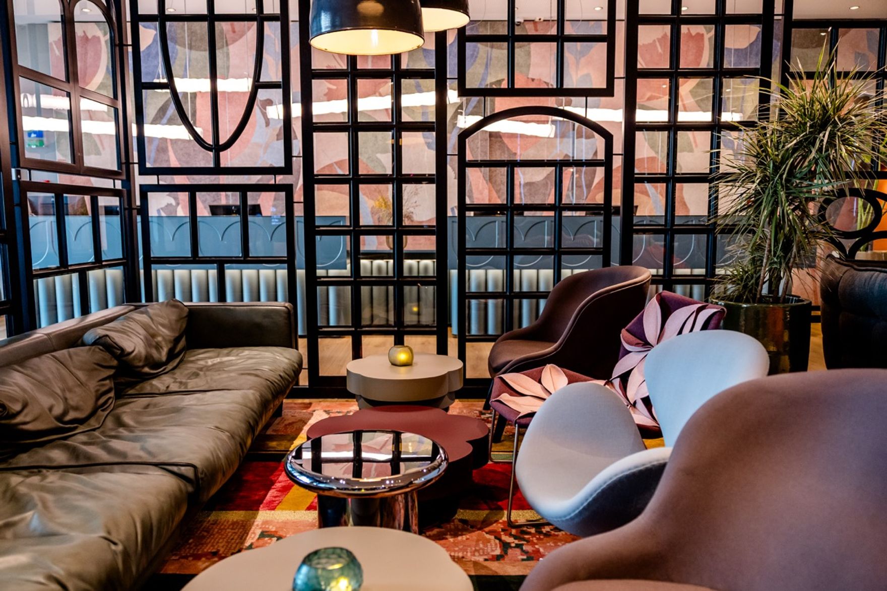Elegante Lounge mit bequemen Sesseln, einem Ledersofa und dekorativen Trennwänden, durch die gedämpftes Tageslicht fällt – ideal für entspannte Gespräche oder kurze Pausen.