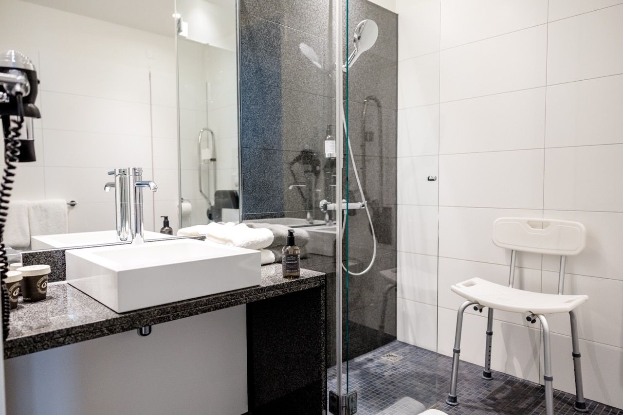 Modernes Badezimmer mit barrierefreier Dusche, Duschstuhl und großem Spiegel. Helle, freundliche Atmosphäre mit klaren Linien und funktionaler Ausstattung.