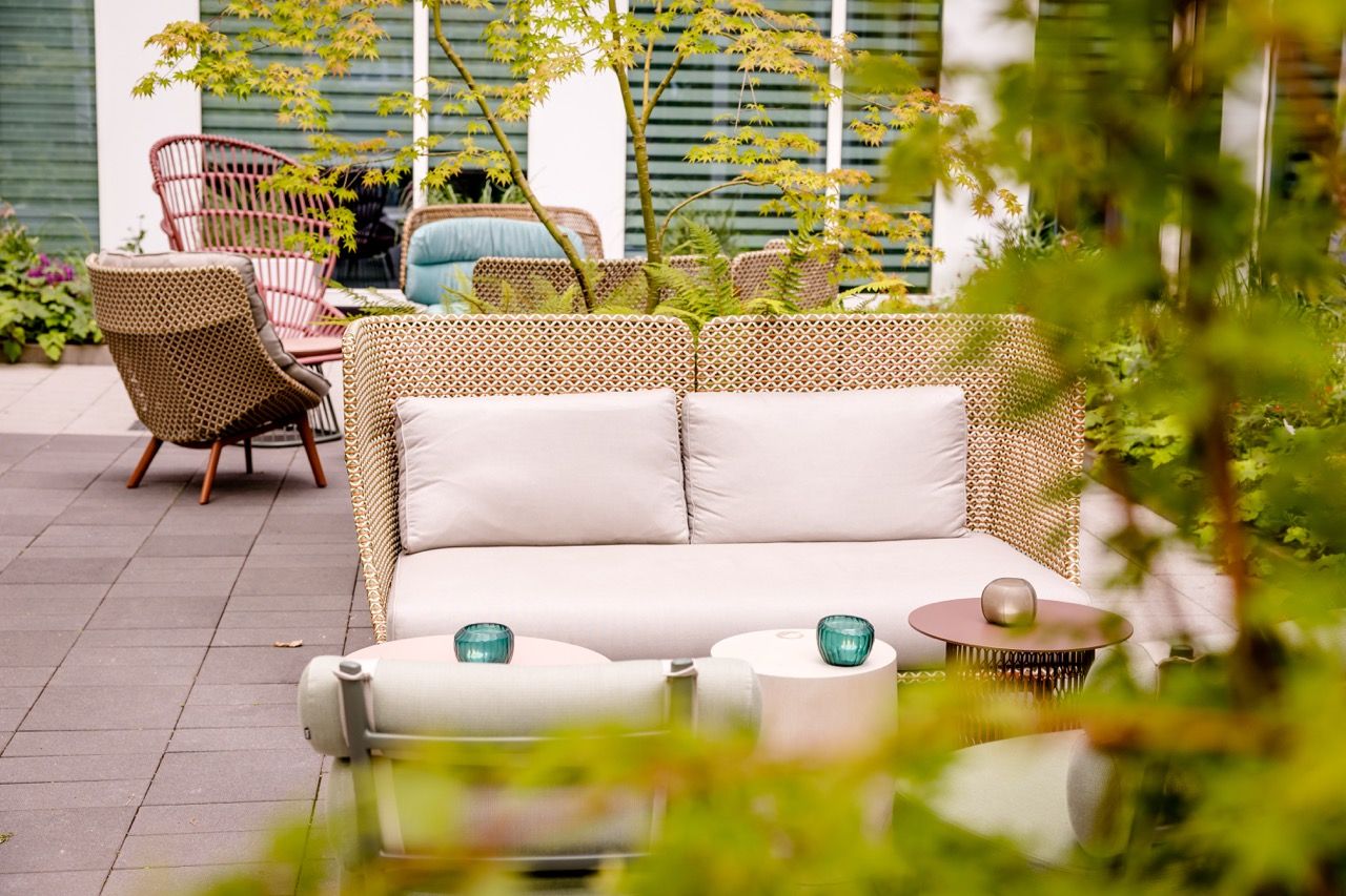 Gemütliche, moderne Außensitzgruppe mit Polstersofa und Stühlen auf Terrasse, umgeben von grünen Pflanzen, ideal zum Entspannen und Genießen ruhiger Momente.
