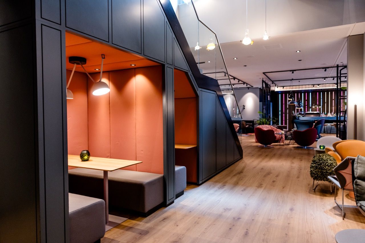 Moderner Lounge-Bereich mit gemütlichen Sitznischen in warmen Farben, stilvollen Sesseln und Holzboden, ideal zum Entspannen oder Arbeiten in ruhiger Atmosphäre. Sanfte Beleuchtung unterstreicht das einladende Ambiente.
