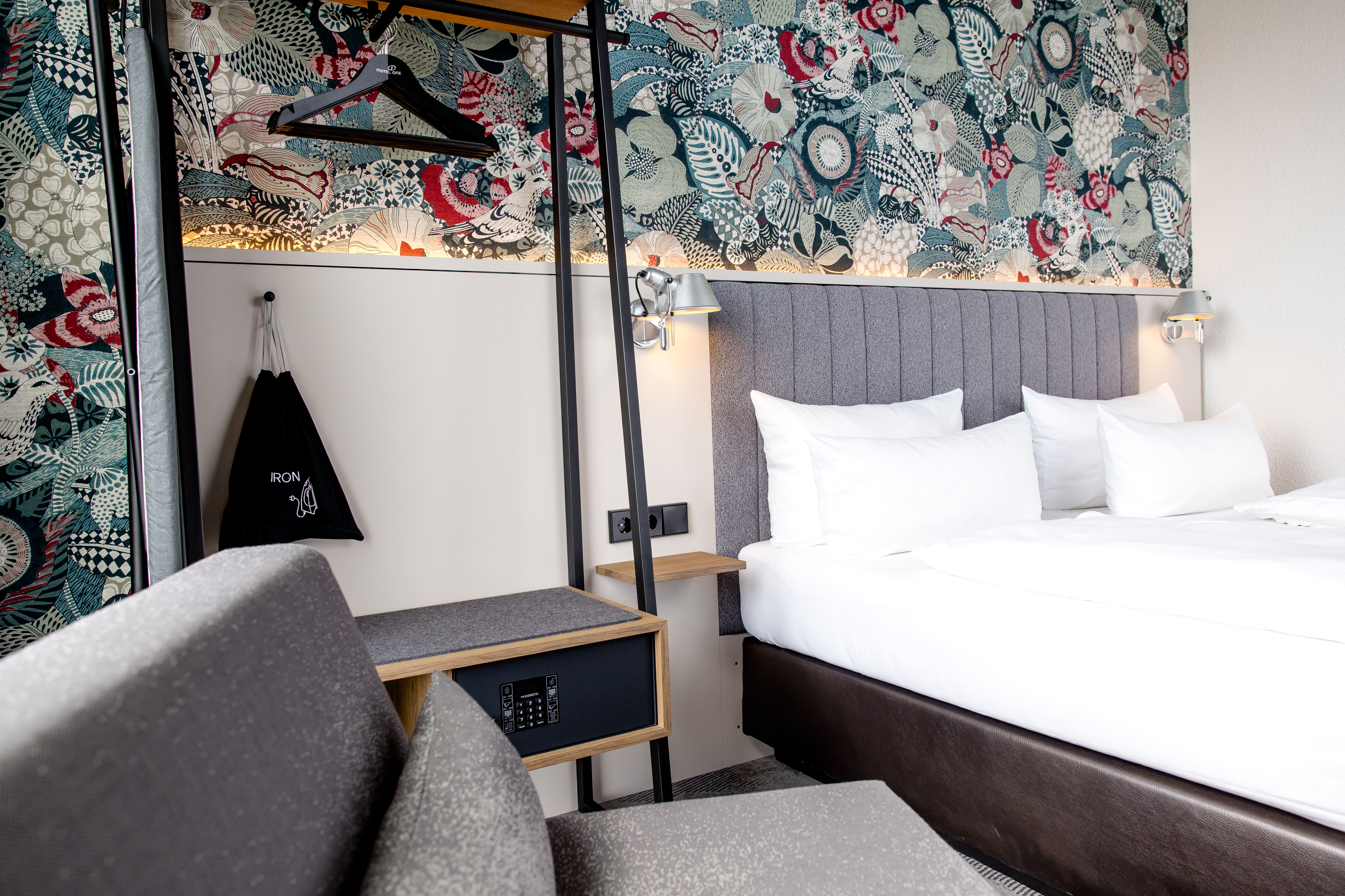 Modern eingerichtetes Hotelzimmer mit großzügigem Doppelbett, gemütlicher Sitzecke, elegantem Muster an der Wand und funktionalem Kleiderschrank mit Spiegel und Safe für Komfort und Sicherheit während des Aufenthalts. Modern eingerichtetes Hotelzimmer mit großzügigem Doppelbett, gemütlicher Sitzecke, elegantem Muster an der Wand und funktionalem Kleiderschrank mit Spiegel und Safe für Komfort und Sicherheit während des Aufenthalts.