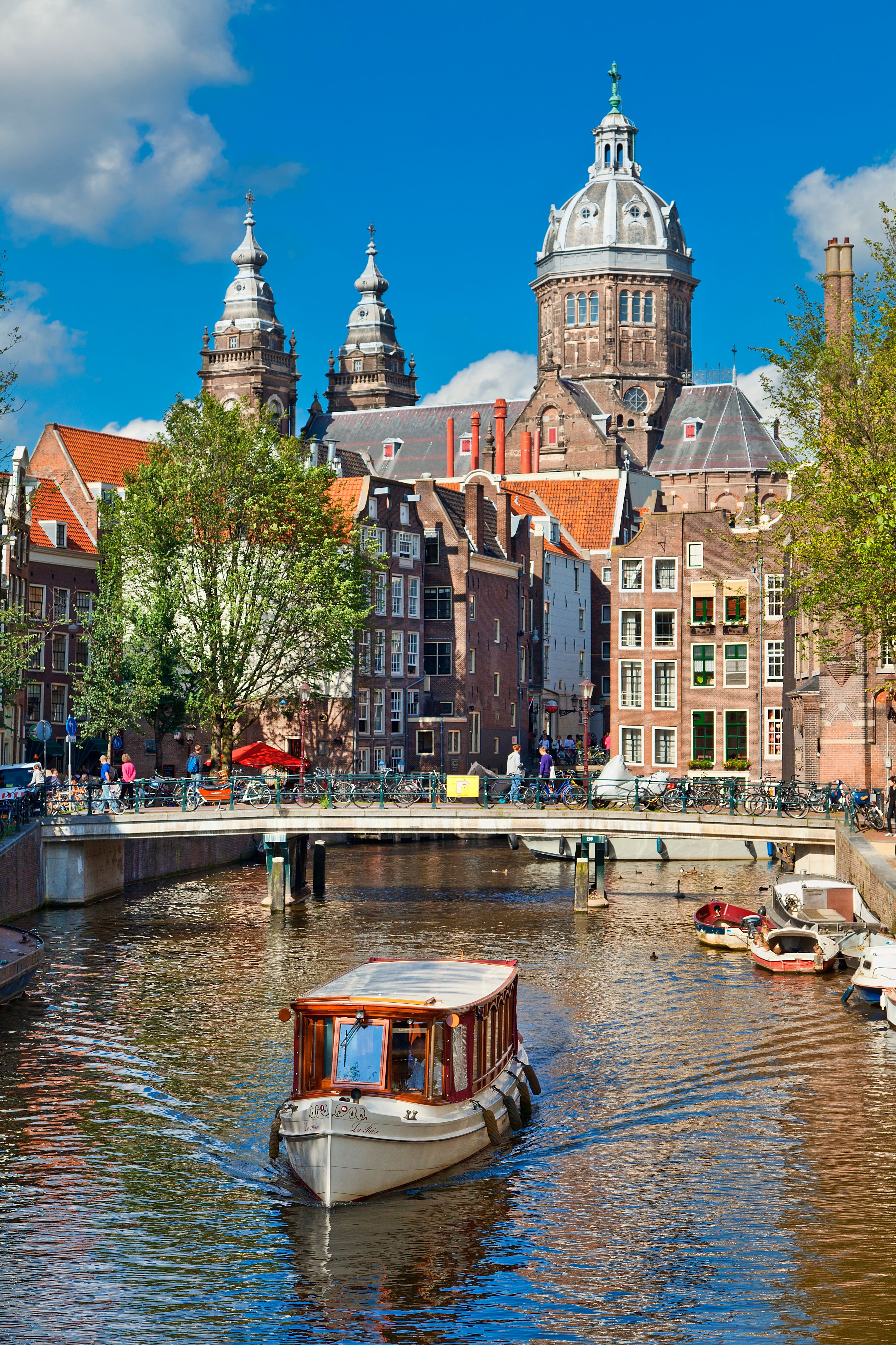 Blick auf einen historischen Stadtkanal mit einem kleinen Bootsfahrgastschiff, umgeben von klassischen Gebäuden und Türmen unter blauem Himmel, typisch für eine europäische Stadt mit reicher Architektur und Wasserwegen.