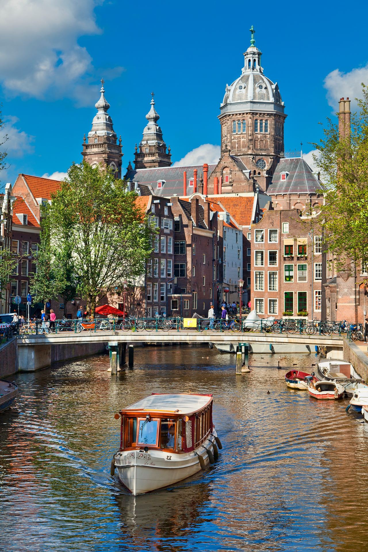 Blick auf einen historischen Stadtkanal mit einem kleinen Bootsfahrgastschiff, umgeben von klassischen Gebäuden und Türmen unter blauem Himmel, typisch für eine europäische Stadt mit reicher Architektur und Wasserwegen.