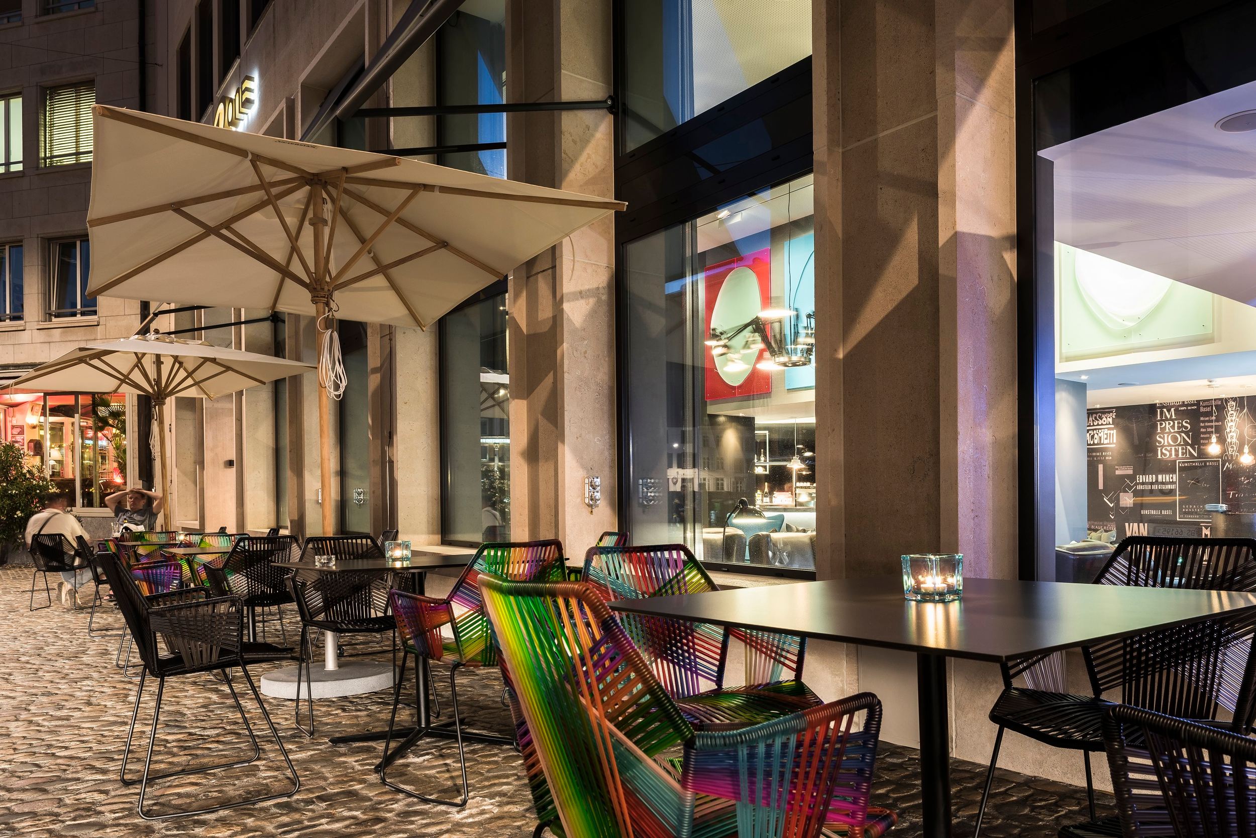 Hotel Basel Motel One Außenbereich mit mehreren Sitzgelegenheiten bei Abend