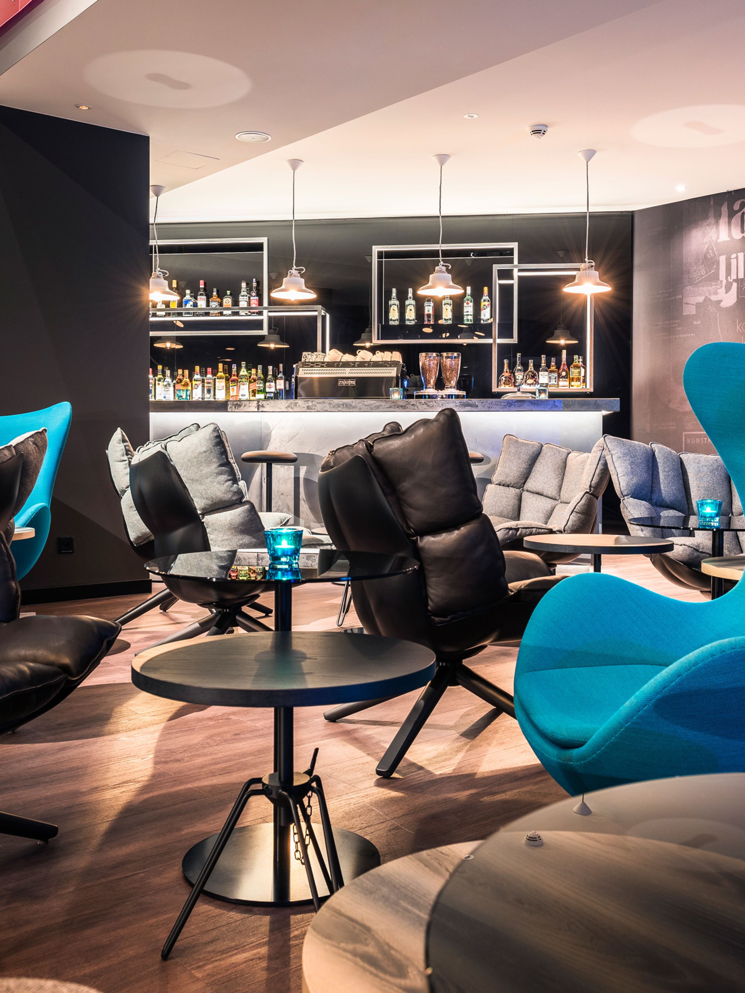 Designhotel Basel Motel One Lounge mit Egg Chair und weiteren Stühlen im Vordergrund sowie Bar im Hintergrund