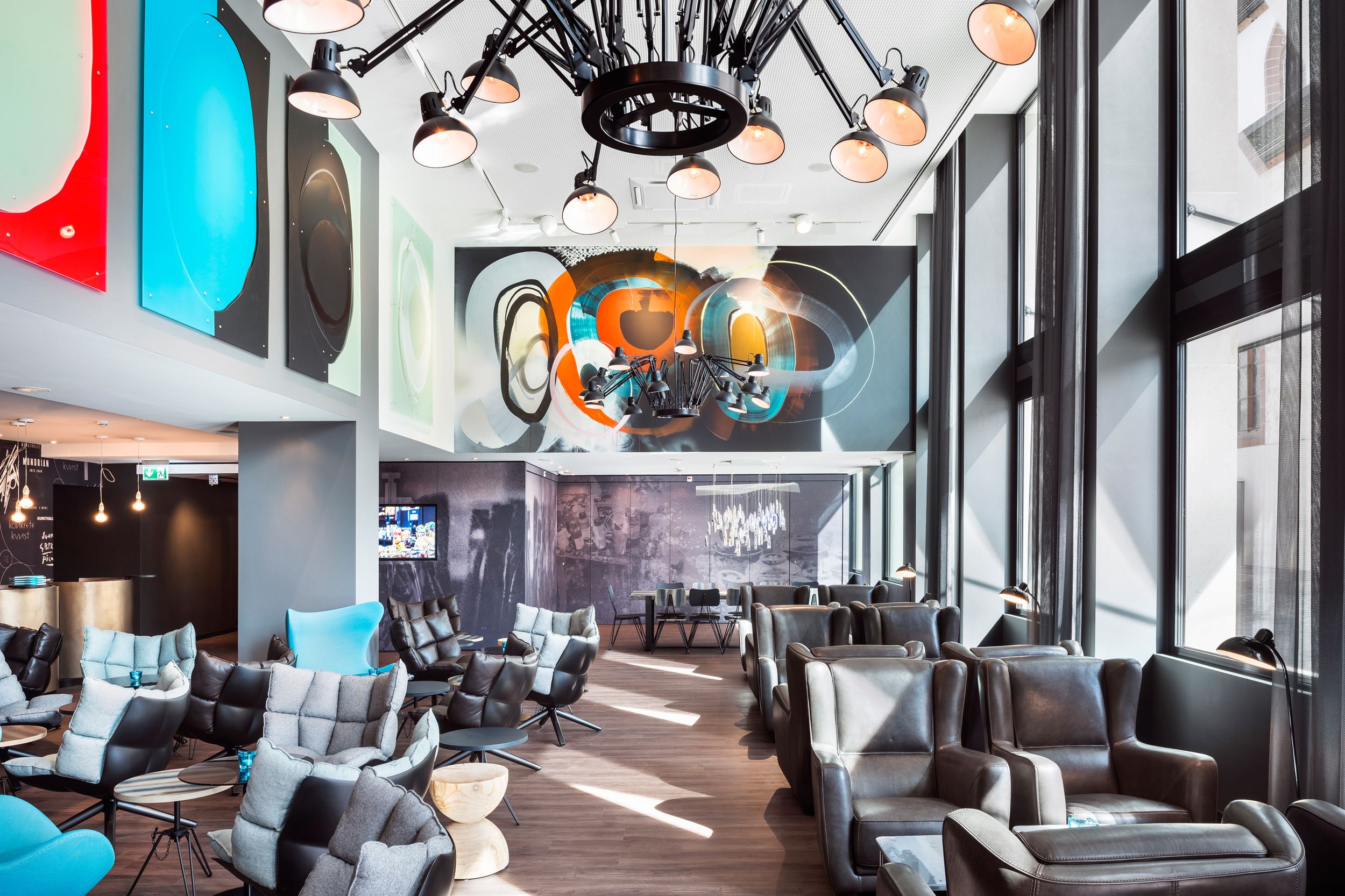 Designhotel Basel Motel One Lounge mit Sonneneinstrahlung durch bodentiefe Fenster und mehrere Sitzgelegenheiten
