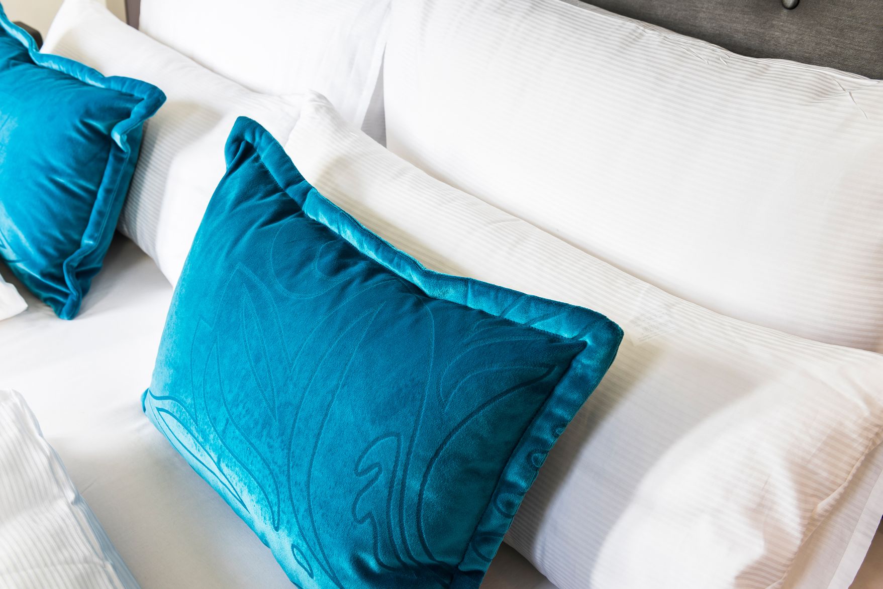 Designhotel Basel Motel One Nahaufnahme auf ein Doppelbett mit vier weißen Kissen sowie zwei Zierkissen in türkis