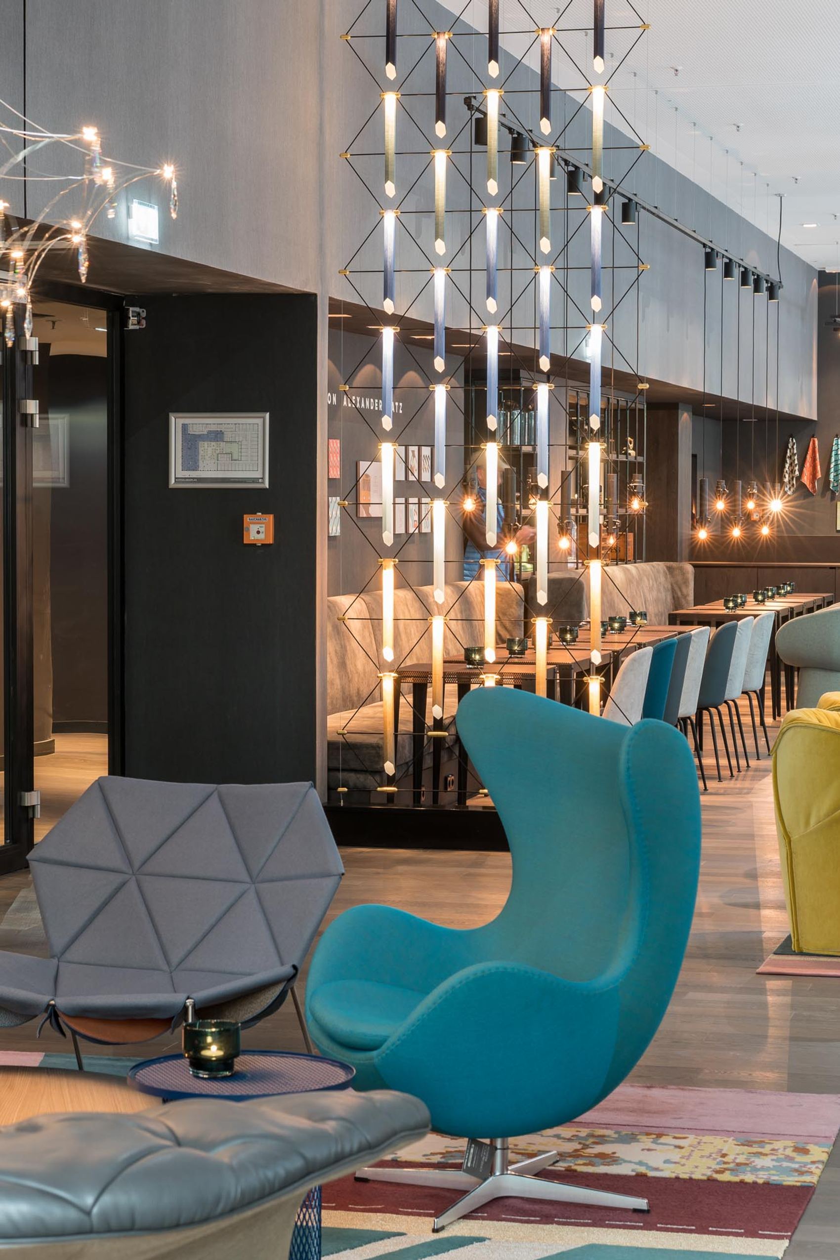 Hotel Berlin Alexanderplatz Motel One lichtdurchflutete Lounge mit mehreren Sitzgelegenheiten und ein Egg Chair in türkis im Vordergrund