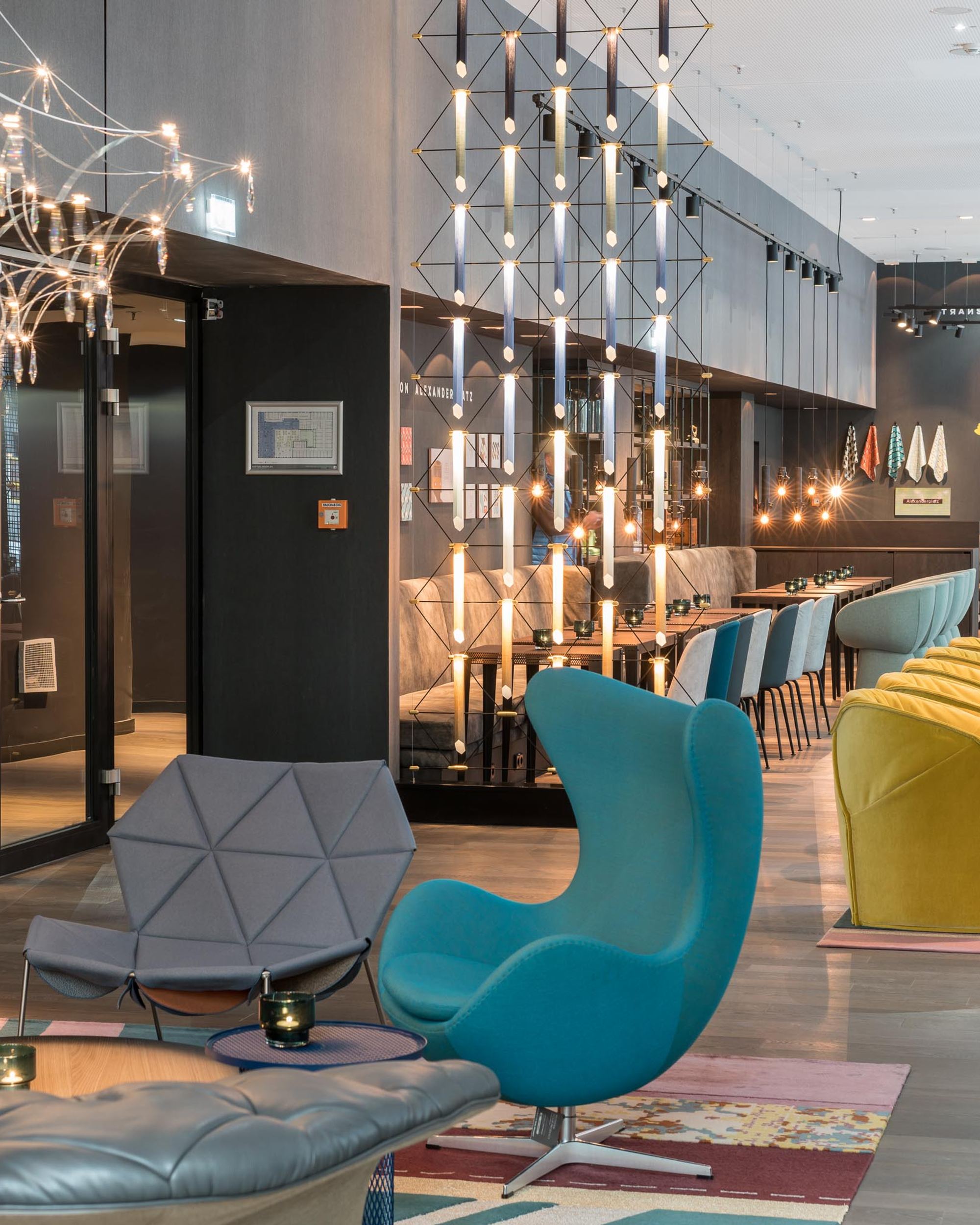 Hotel Berlin Alexanderplatz Motel One lichtdurchflutete Lounge mit mehreren Sitzgelegenheiten und ein Egg Chair in türkis im Vordergrund
