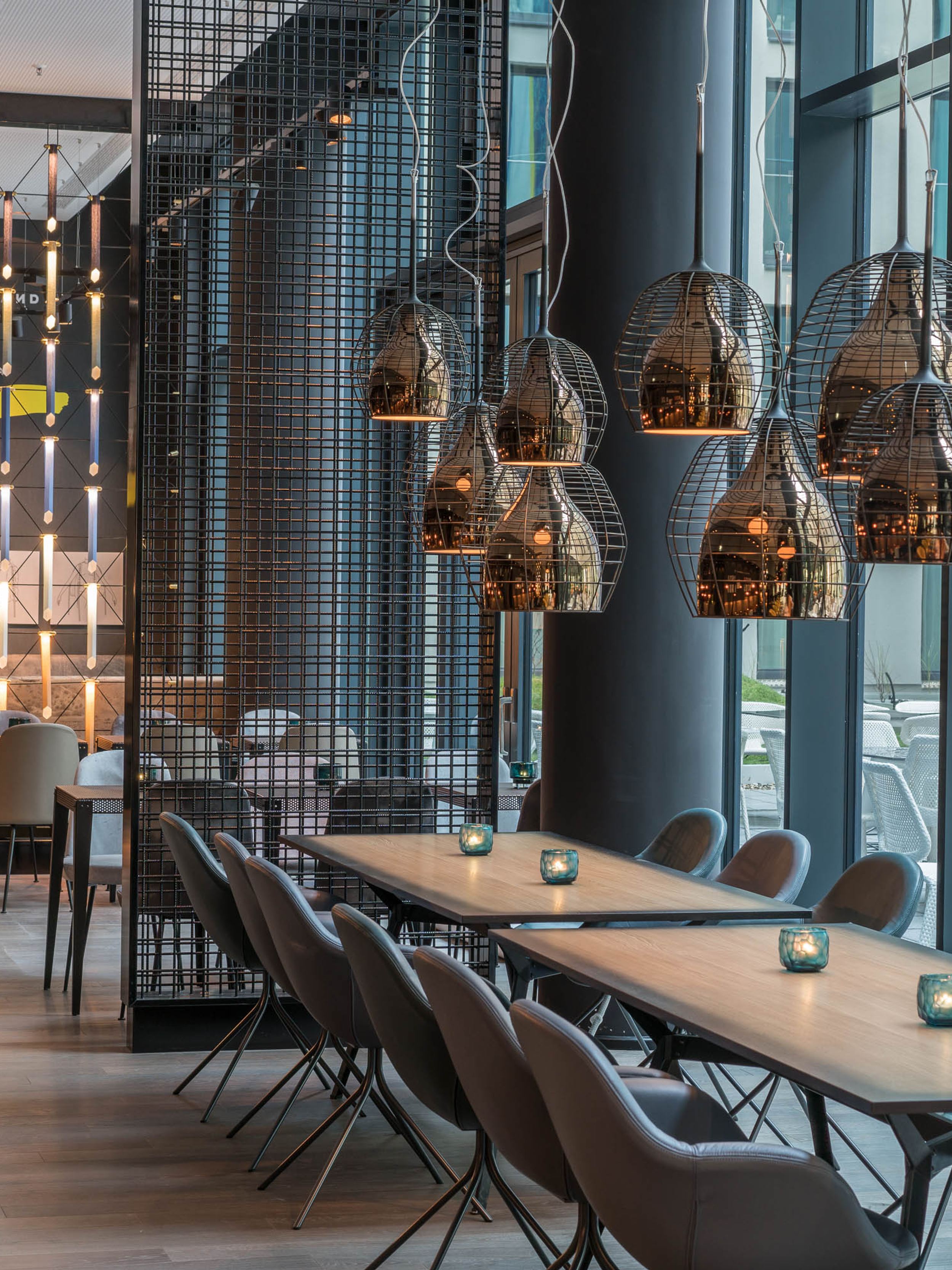 Hotel Berlin Alexanderplatz Motel One helle Lounge mit Tischen und Stühlen sowie große Fensterfront mit Blick auf den Außenbereich des Hotels mit weiteren Sitzgelegenheiten