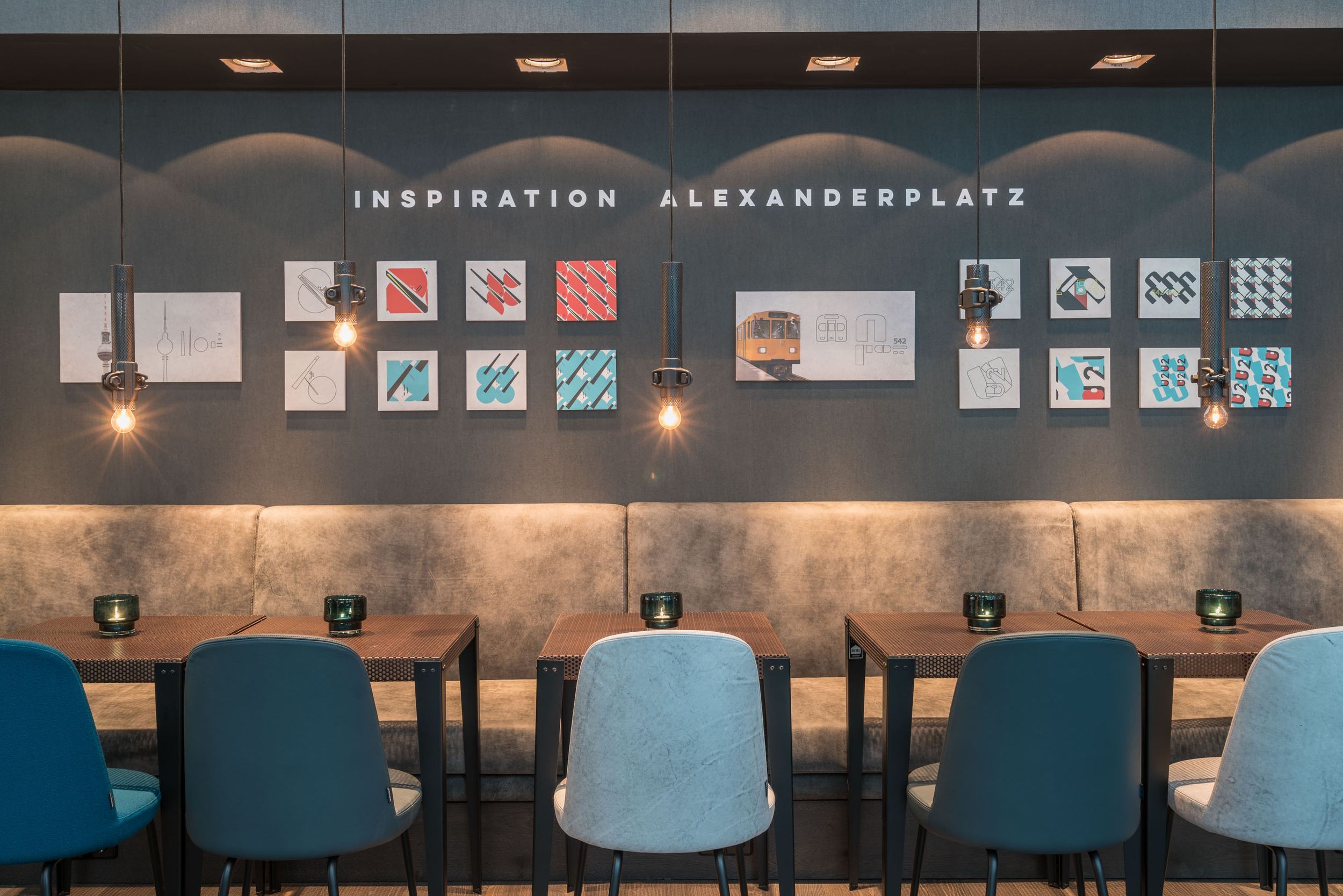 Hotel Berlin Alexanderplatz Motel One Essbereich mit mehreren Tischen und Stühlen sowie Schriftzug Inspiration Alexanderplatz an der Wand