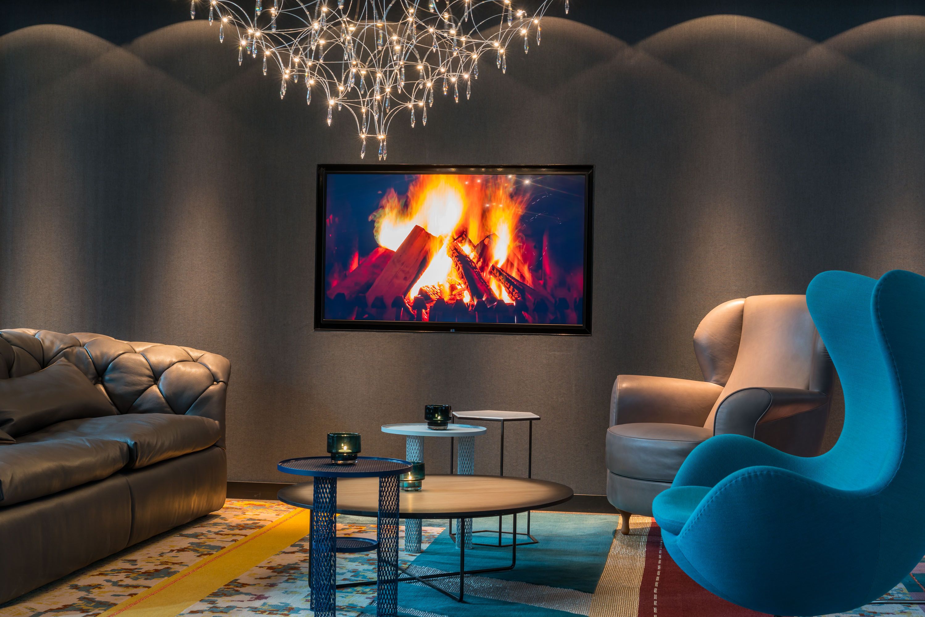Designhotel Berlin Alexanderplatz Motel One Lounge mit Sofa, Sessel und Egg Chair sowie Fernseher mit Bild von Feuer an der Wand