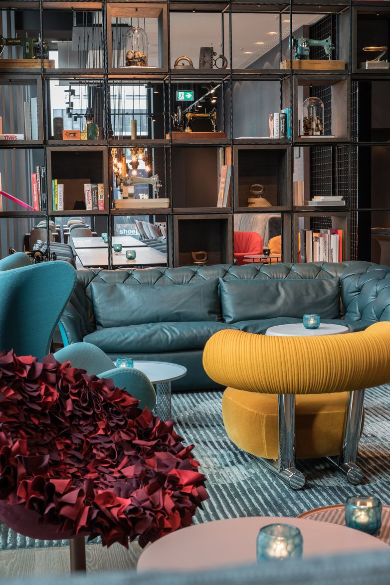 Hotel Berlin Alexanderplatz Motel One lichtdurchflutete Lounge mit großem Sofa, Sesseln, Egg Chair sowie offenes Regal mit Dekoration