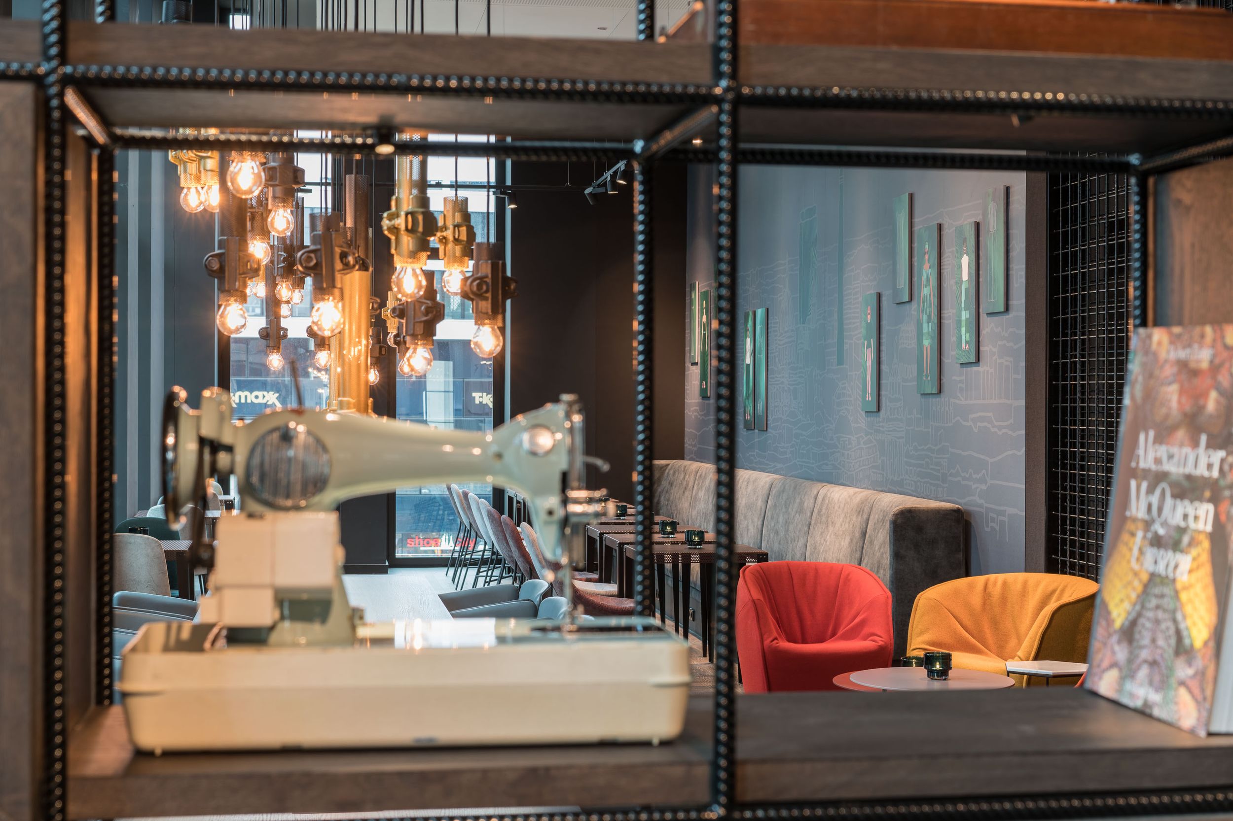 Hotel Berlin Alexanderplatz Motel One Lounge mit Sitzgelegenheiten und Blick auf eine Nähmaschine im Vordergrund in einem offenen Regal