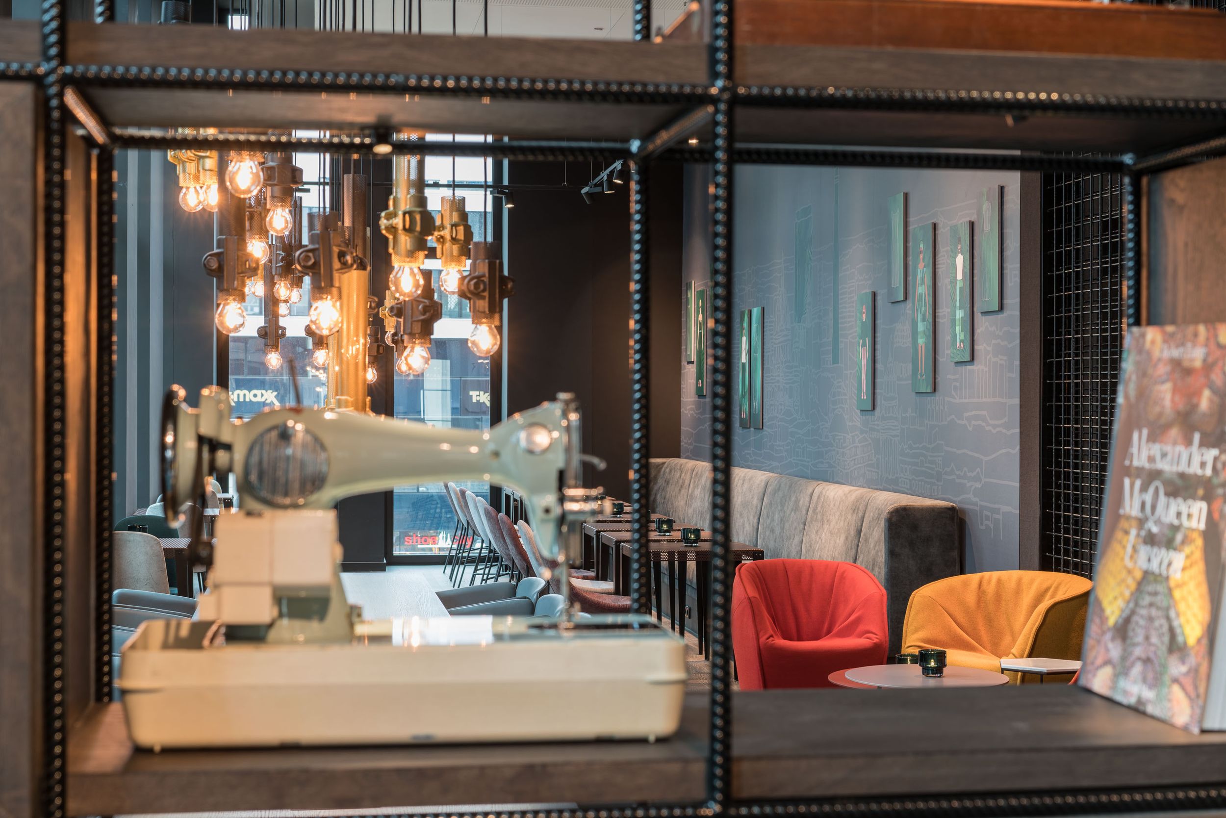 Hotel Berlin Alexanderplatz Motel One Lounge mit Sitzgelegenheiten und Blick auf eine Nähmaschine im Vordergrund in einem offenen Regal