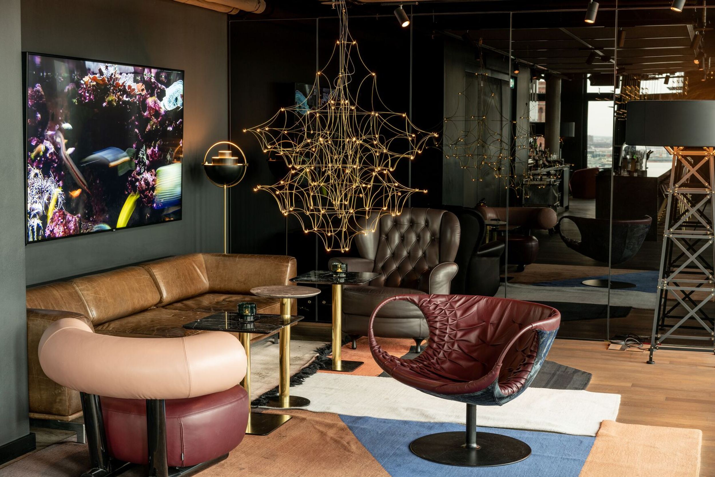 Hotel Berlin Alexanderplatz Motel One helle Lounge mit Blick auf eine Sitzgruppe bestehend aus einem Sofa und drei Sesseln sowie einem Fernseher an der Wand