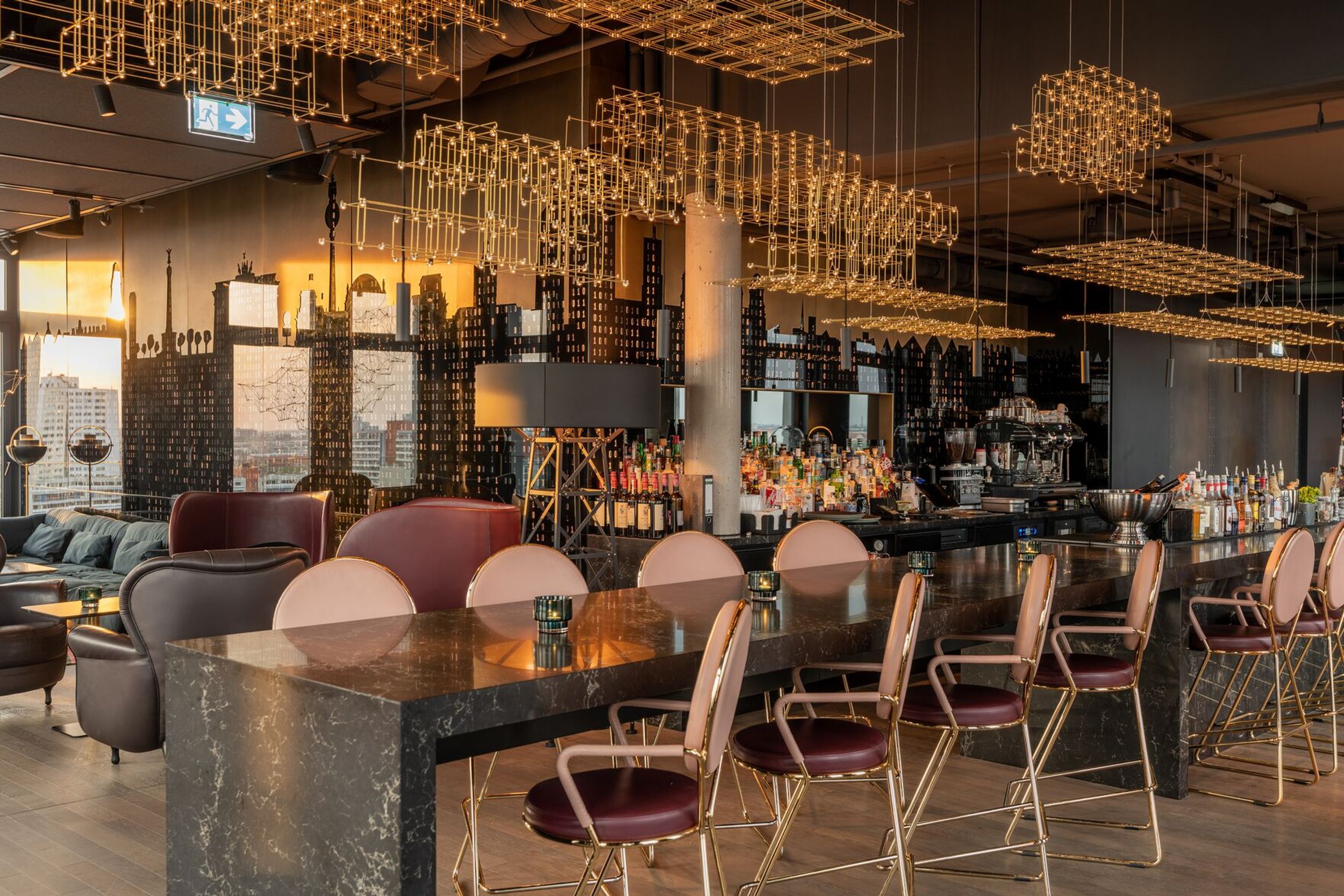 Hotel Berlin Alexanderplatz Motel One helle Lounge mit langem Hochtisch und Stühlen im Vordergrund sowie Bar im Hintergrund