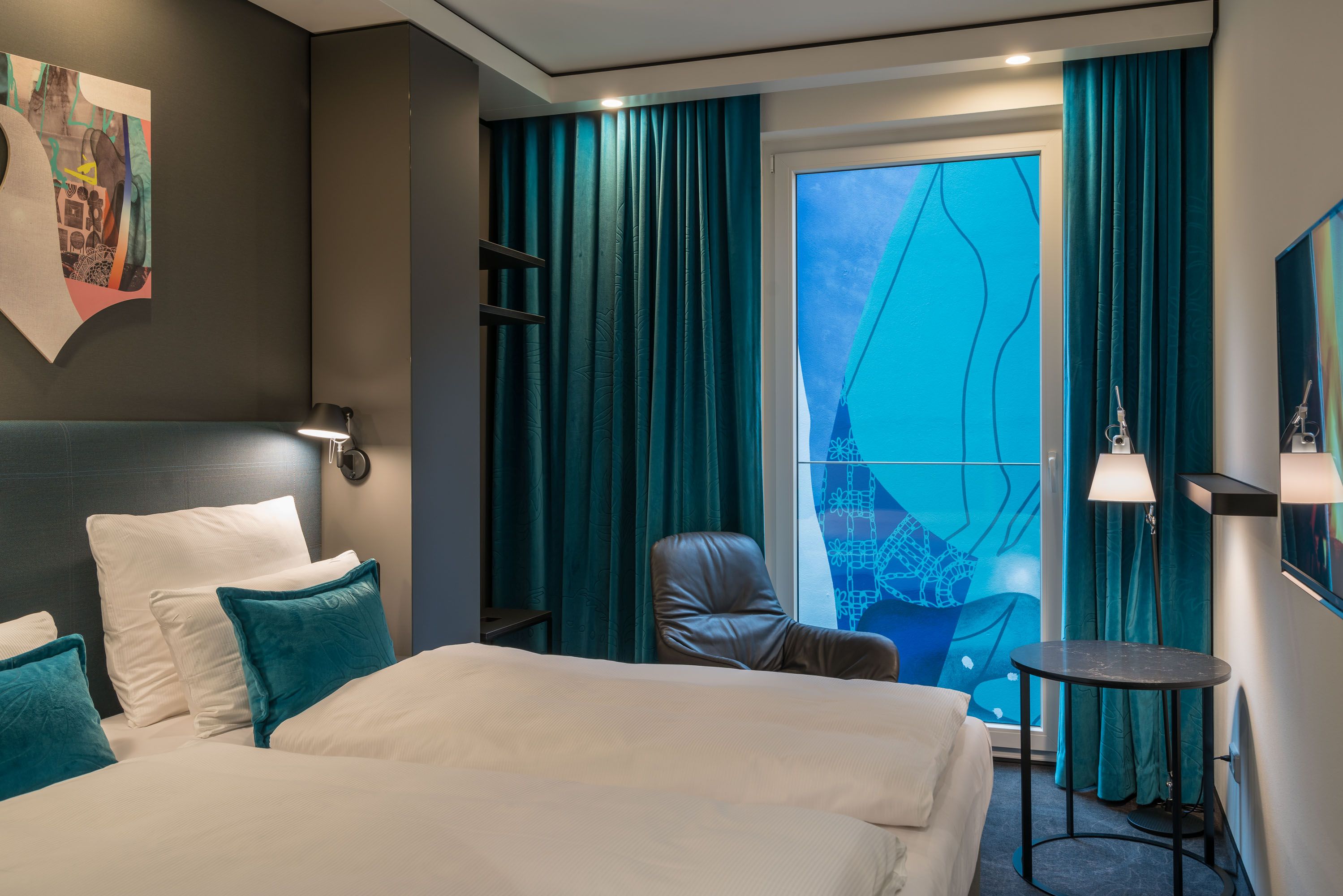 Hotel Berlin Alexanderplatz Motel One seitlicher Blick in ein Zimmer mit Doppelbett und Sessel vor bodentiefem Fenster