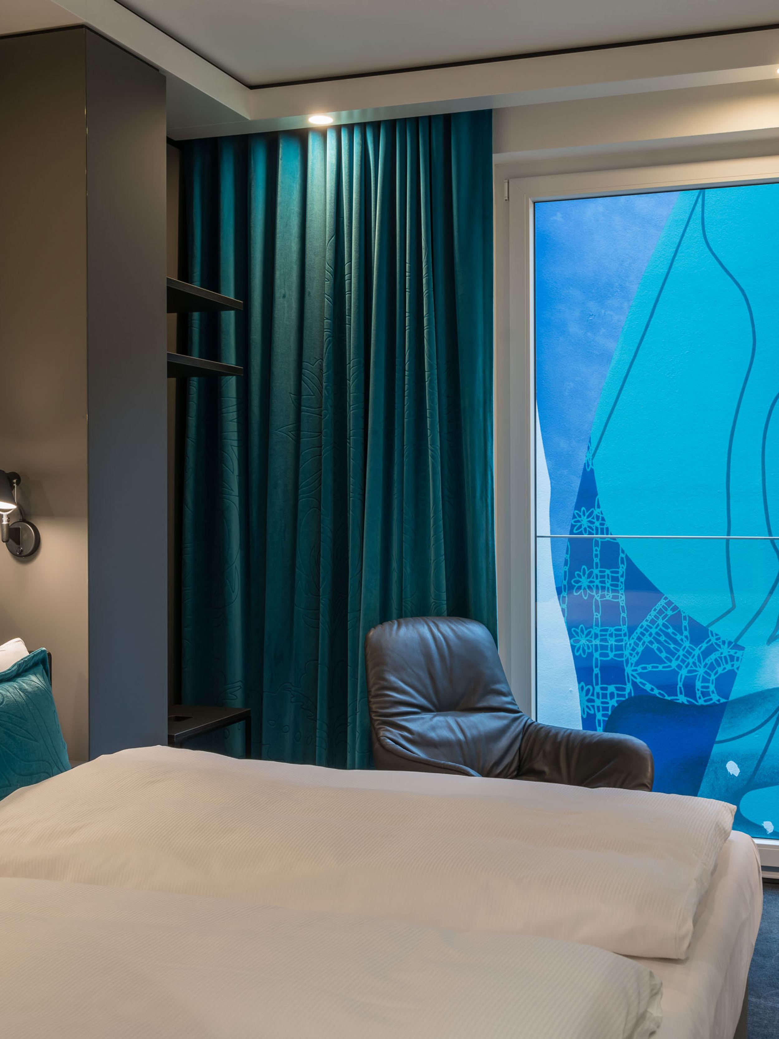 hotel Berlin Alexanderplatz Motel One side view of a room with a double bed and armchair in front of a floor-to-ceiling window