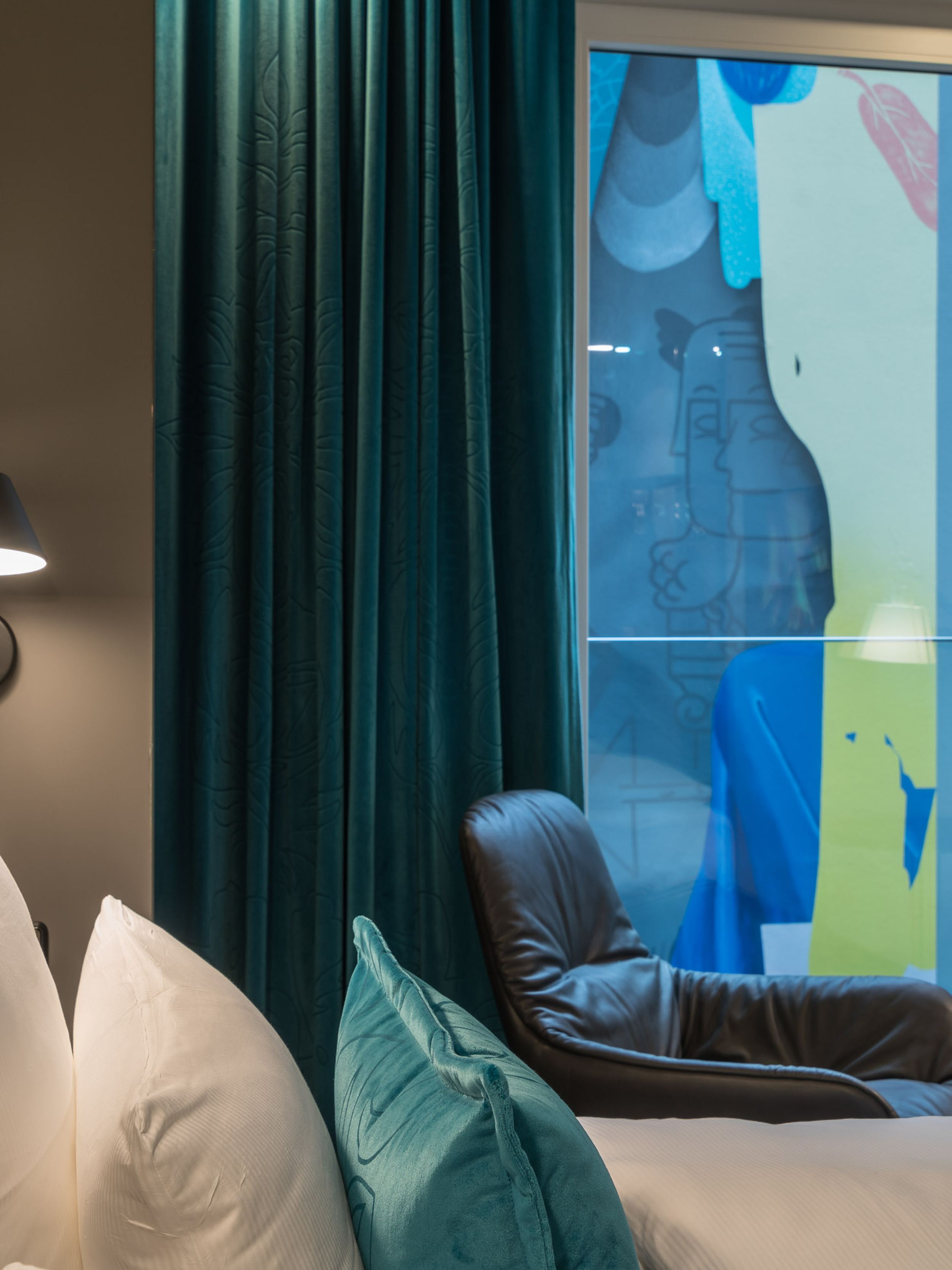 Designhotel Berlin Alexanderplatz Motel One Zimmer mit Blick über ein Doppelbett auf einen Sessel vor einem großen Fenster