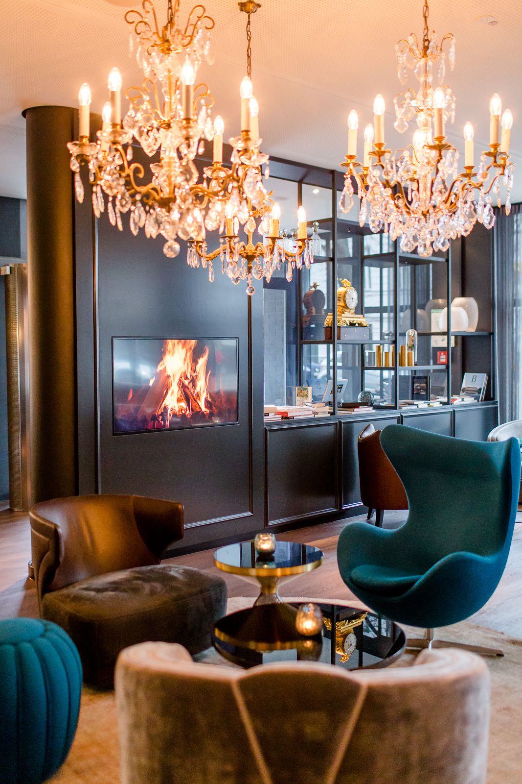 Hotel Berlin Bellevue Motel One lichtdurchflutete Lounge mit Sesseln, Egg Chair, Fernseher an der Wand, Kronleuchter an der Decke und offenem Regal im Hintergrund