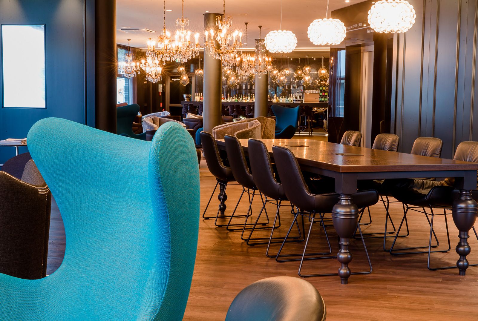 Hotel Berlin Bellevue Motel One helle Lounge mit Egg Chair im Vordergrund, dahinter ein langer Tisch mit Stühlen sowie die Bar im Hintergrund