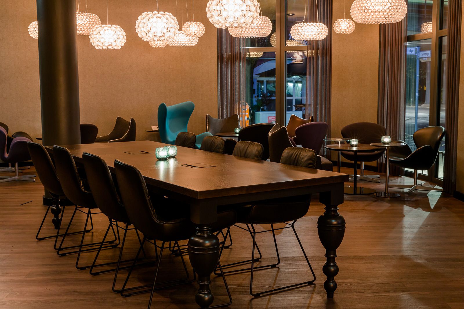 Hotel Berlin Bellevue Motel One Lounge mit langem Tisch und acht Stühlen im Vordergrund sowie mehrere Sessel im Hintergrund vor bodentiefen Fenstern