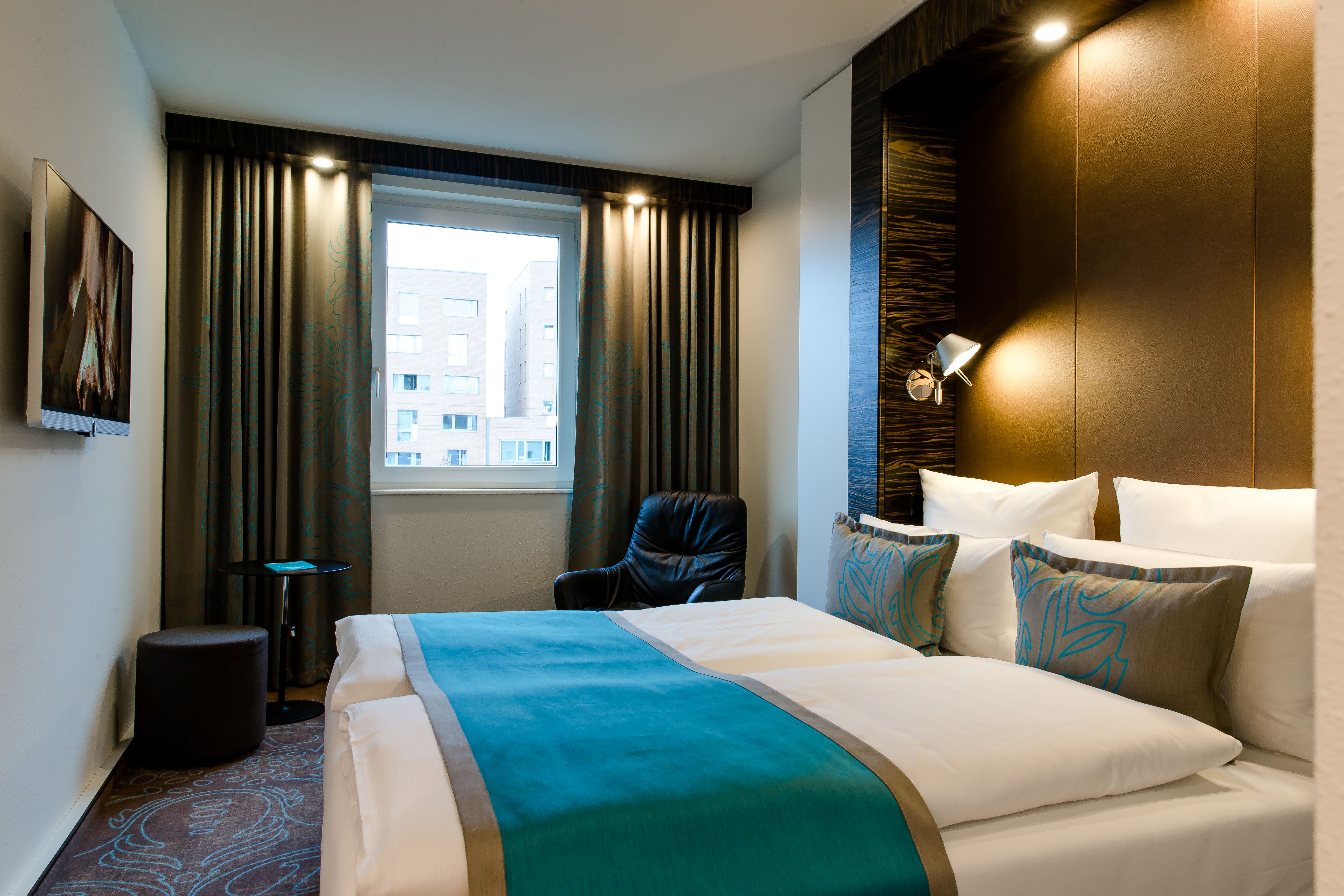 Hotel Berlin Bellevue Motel One helles Zimmer mit großem Doppelbett sowie Sessel vor einem großen Fenster