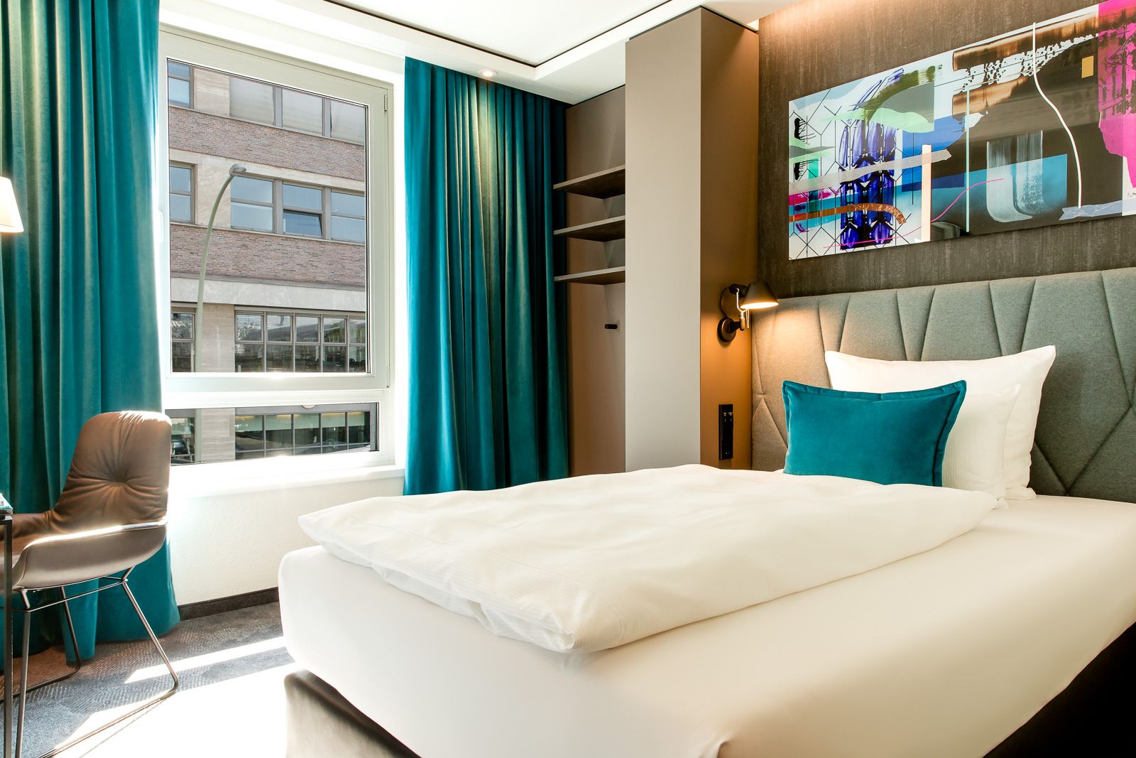 Hotel Berlin Hackescher Markt Motel One lichtdurchflutetes Zimmer mit Einzelbett sowie ein Stuhl vor einem großen Fenster